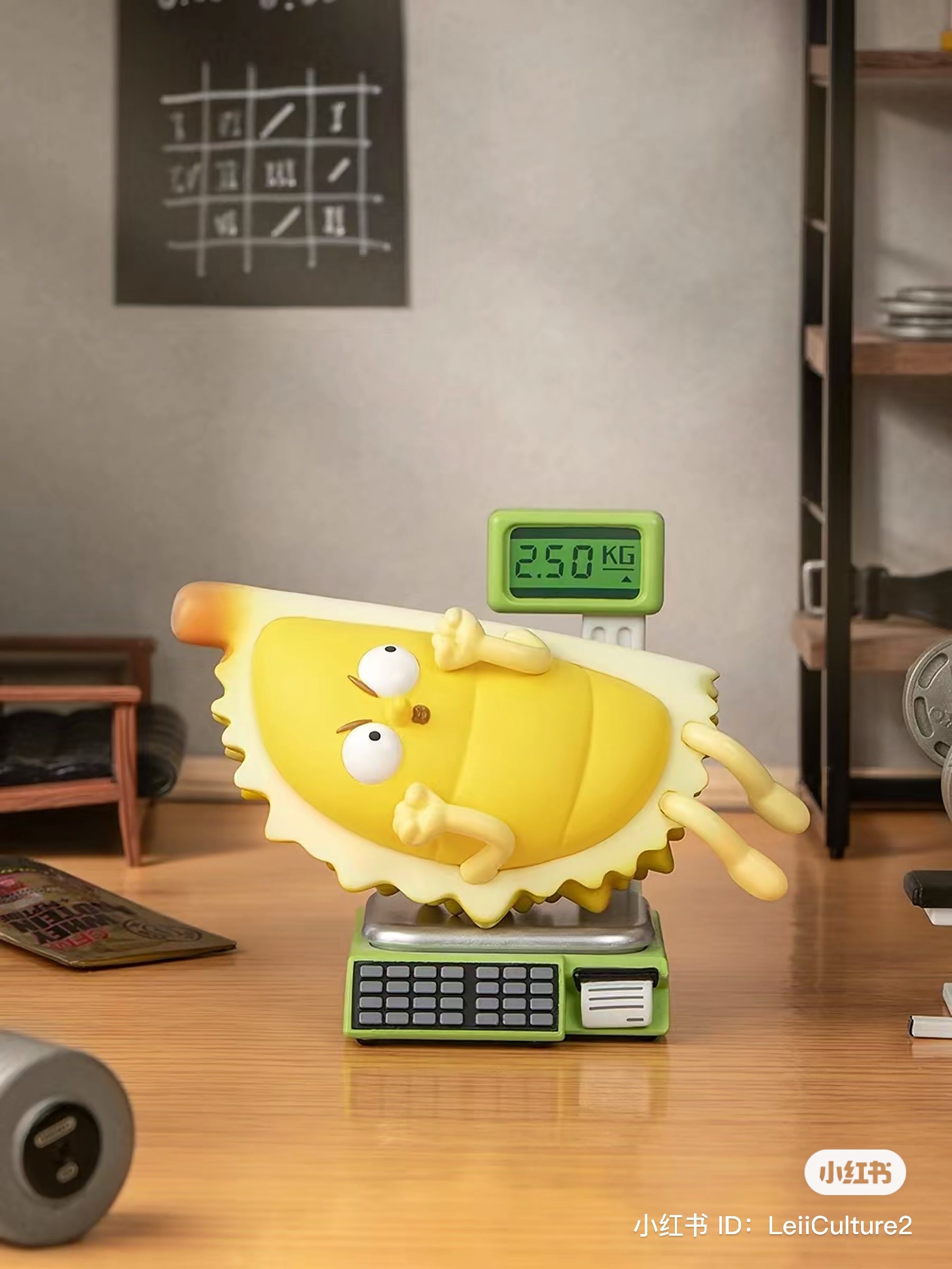 What the Man Daily Blind Box Series toy on a scale with various objects like a chair, fruit, and digital display.