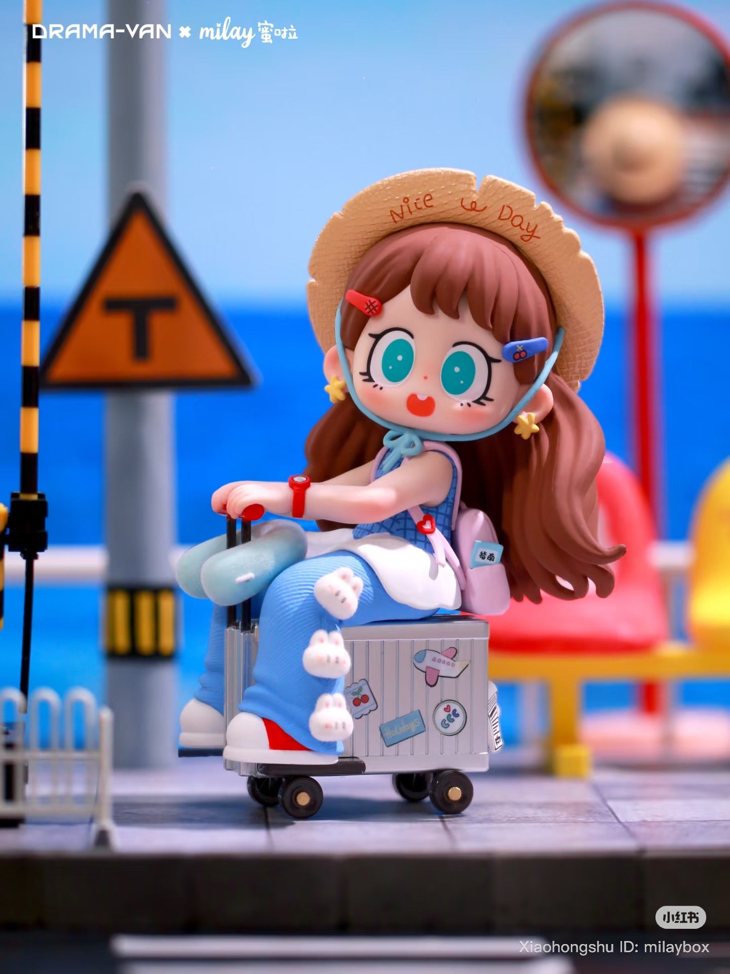 Milay Lazy Time Series Blind Box figurine of a girl on a suitcase, wearing a hat and overalls, set in a seaside station diorama.