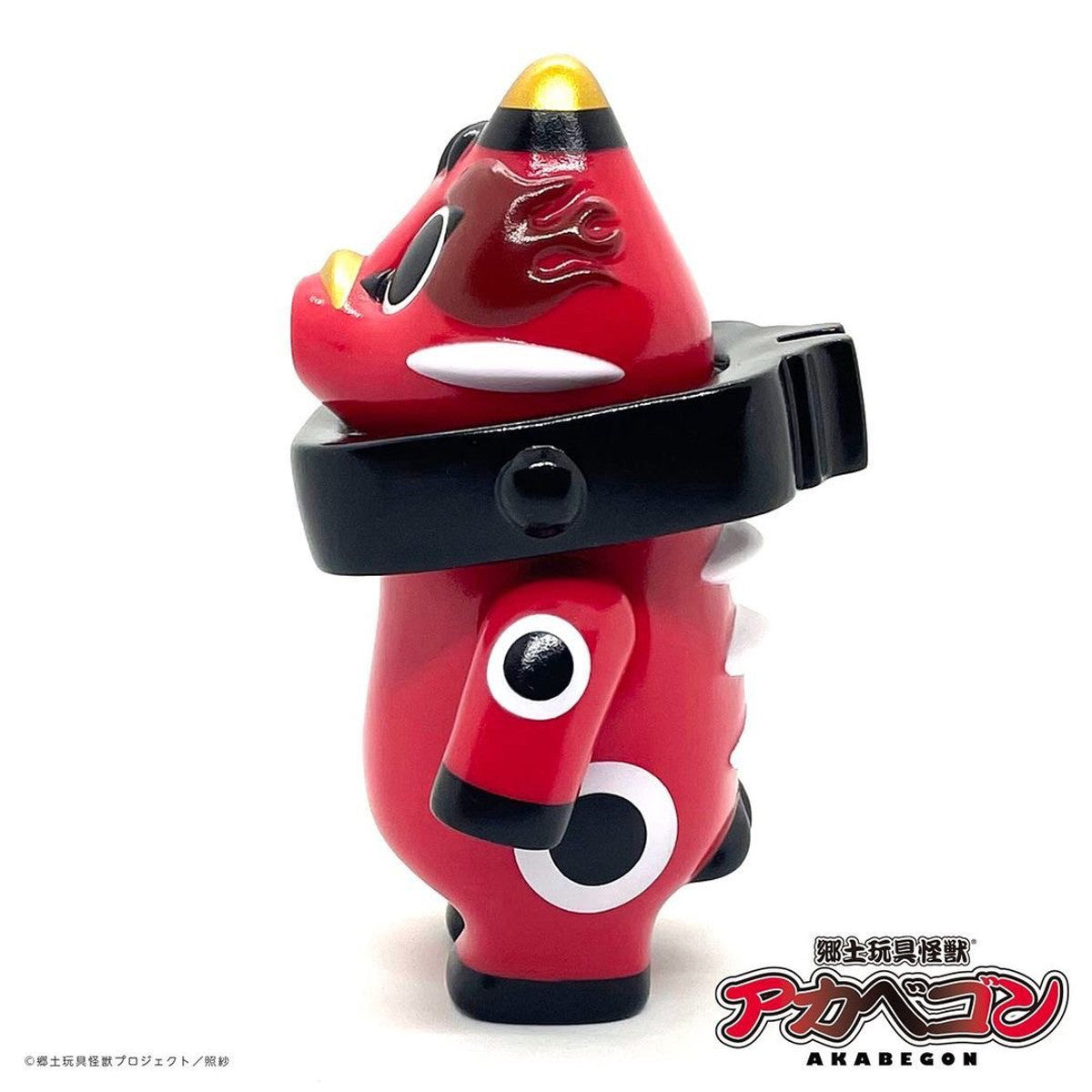 AKABEGON - Red by Teresa Chiba, a 12cm sofubi toy, features a kaiju-inspired design with glossy red vinyl, black-and-white markings, and gold horns.