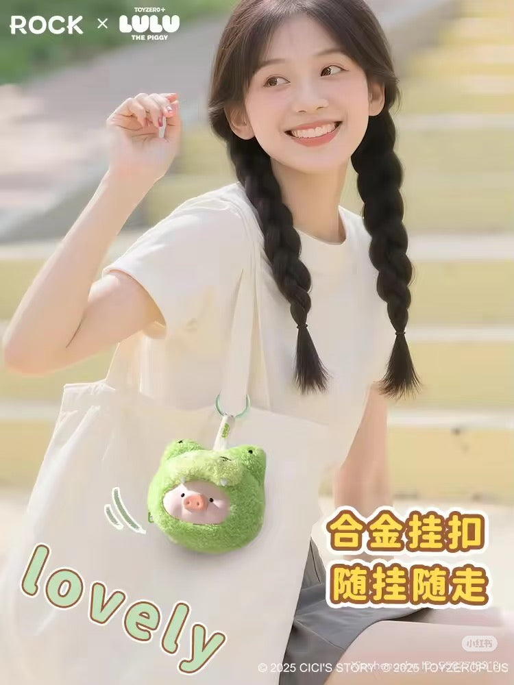 Young woman with braided pigtails smiles, holding a canvas tote with a fuzzy green pig-shaped charm, promoting LuLu the Piggy Animal Party series preorder.
