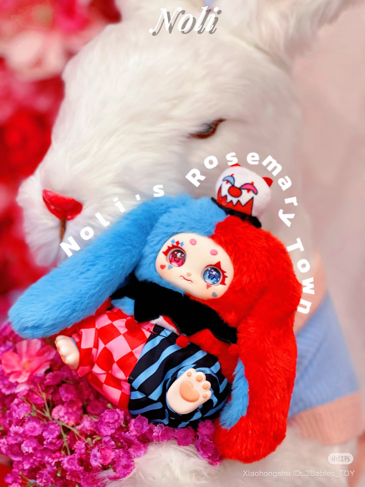 Baby Three - The Rosemary Town of Nori collectible doll with a split bunny-ear hood and harlequin outfit, displayed on purple flowers, available for preorder.