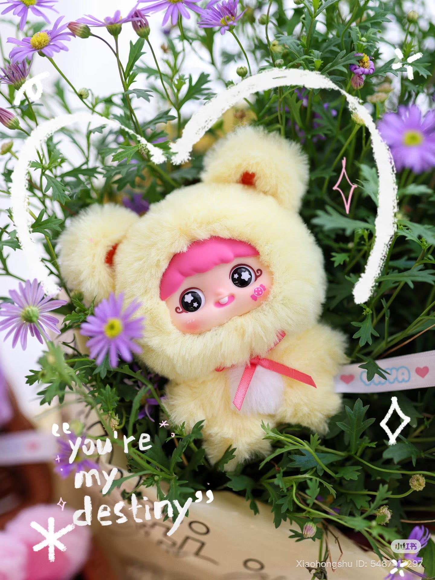 Cartoon-style plush doll in bear outfit among flowers, titled Baby Three - YAYA's first birthday, with sparkly eyes and pink ribbon accent.