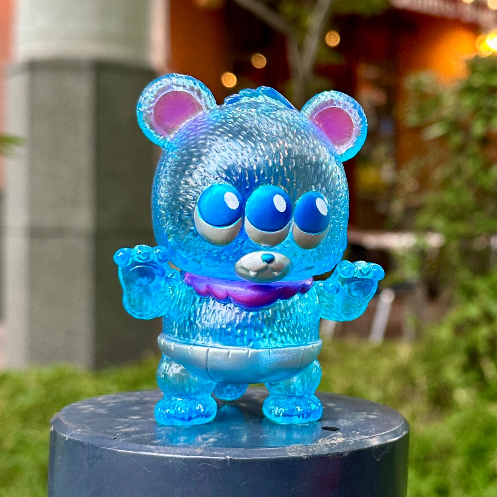 Baby Kumara - CollectedCon Edition by MoMoo Kuma, a limited edition sofubi toy, features three eyes and stands on a black post.