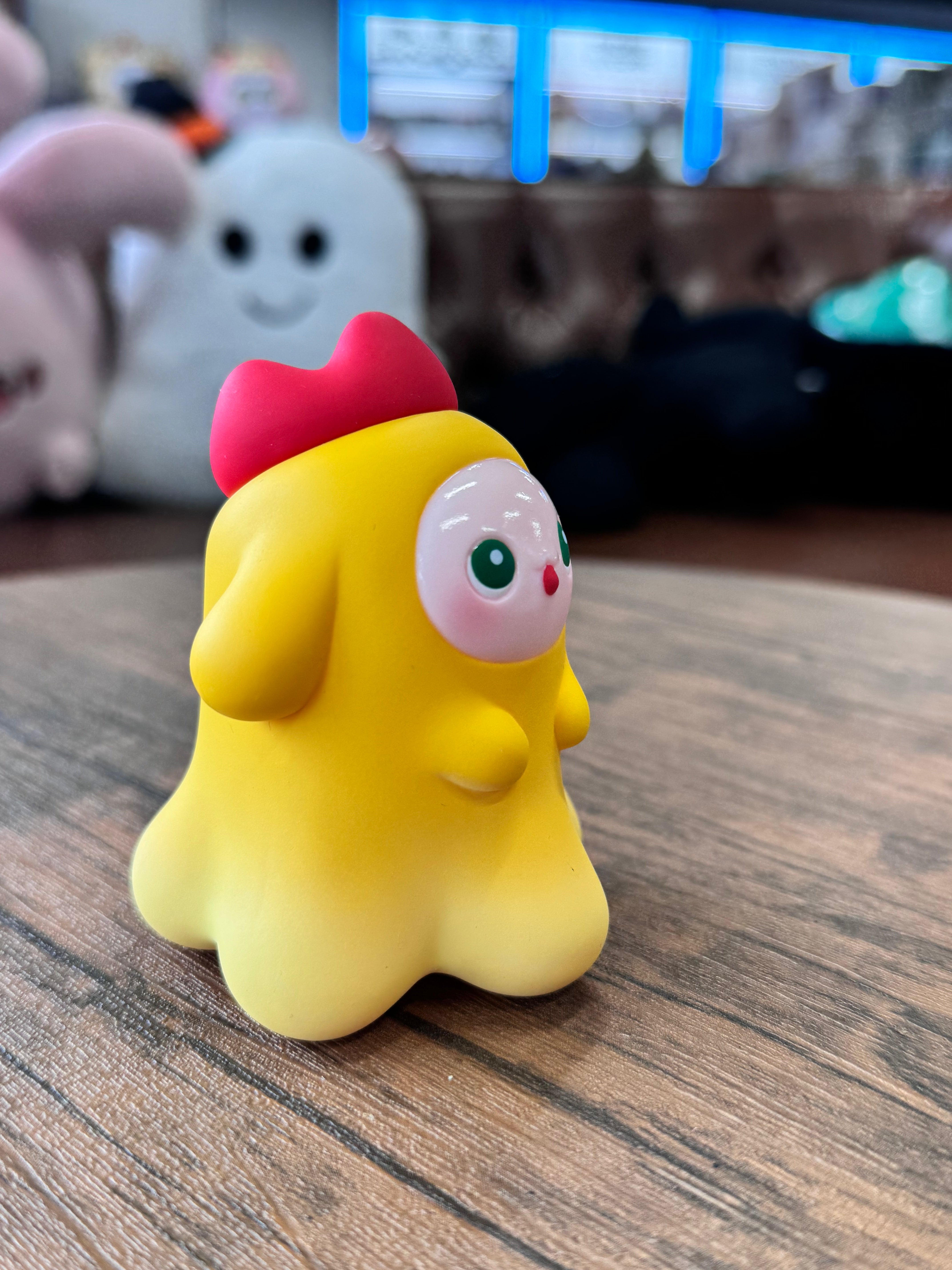 MYONNY - yellow by PYOS: A cartoon-style, yellow vinyl figure with a scalloped base, green eyes, and red heart-shaped crest, showcased on a wood-grain tabletop.