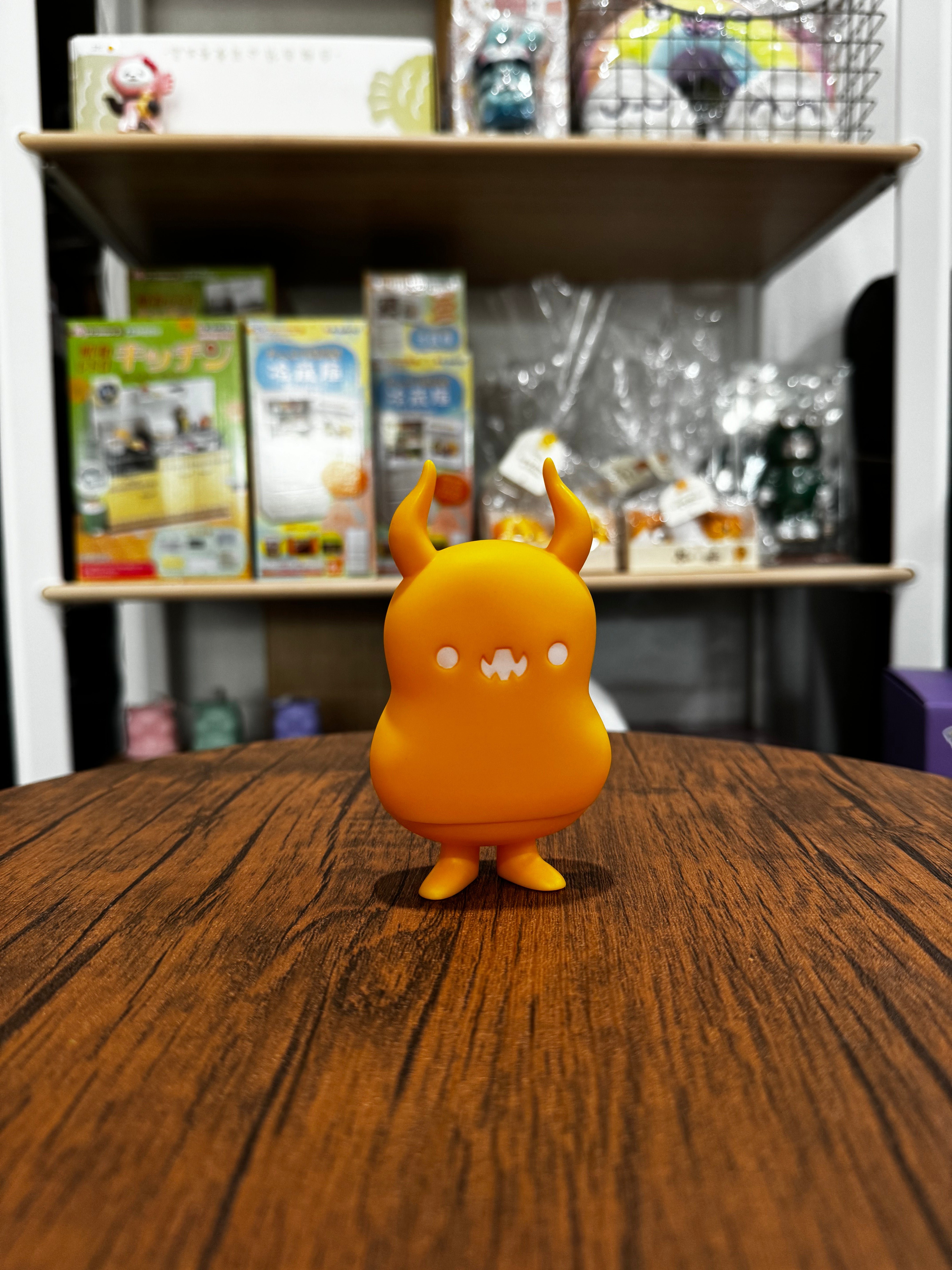 Babababa - Orangesicle by Chishima Konosuke, a yellow toy duck with a face, sits on a table. Japanese Sofubi, 110mm collectible art toy.