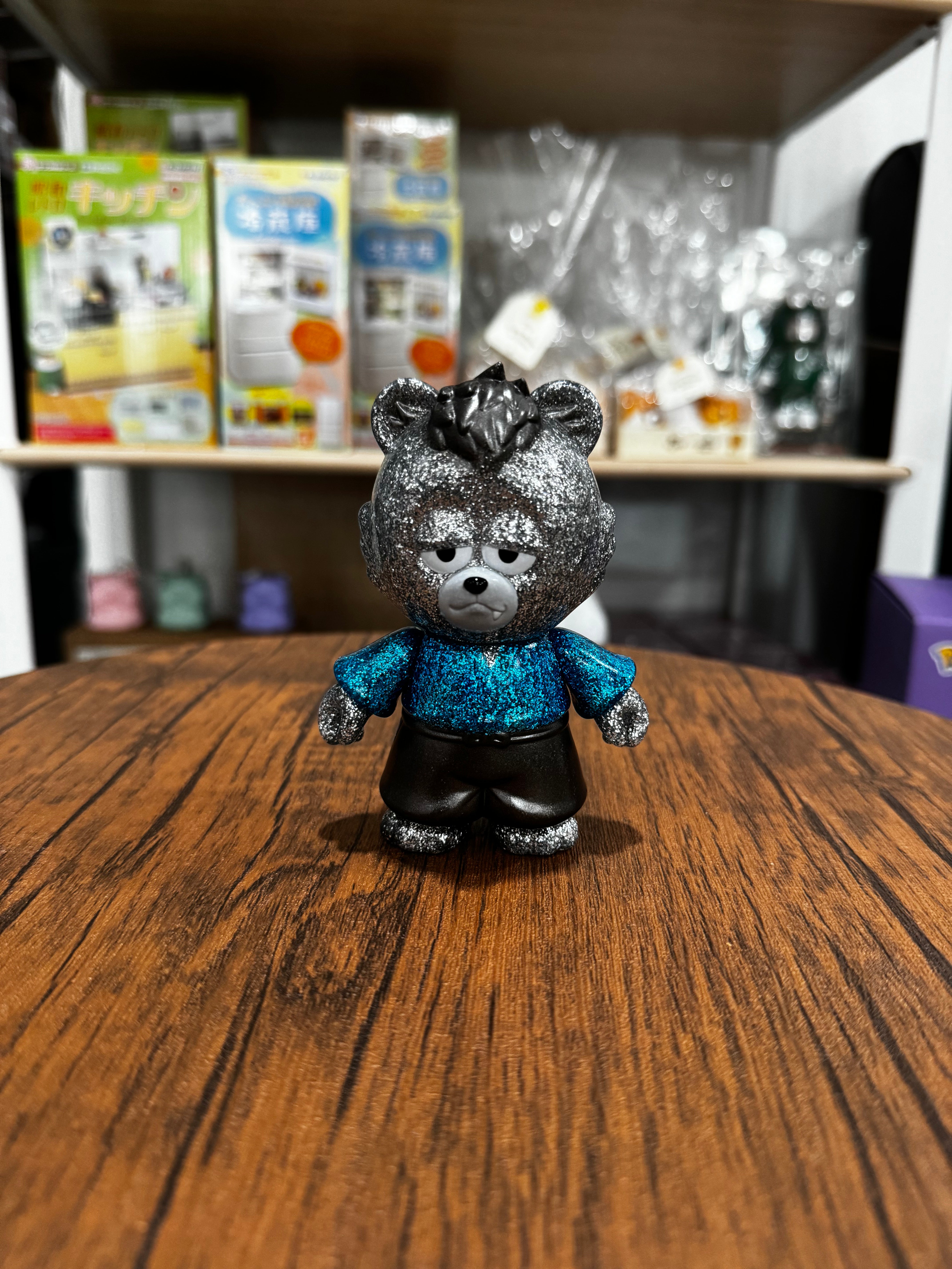 Samurai Bear - Glitter Grizzly by Funky Geek, a 10cm Sofubi toy, sits on a wooden table, showcasing its glittery face and stuffed animal features.