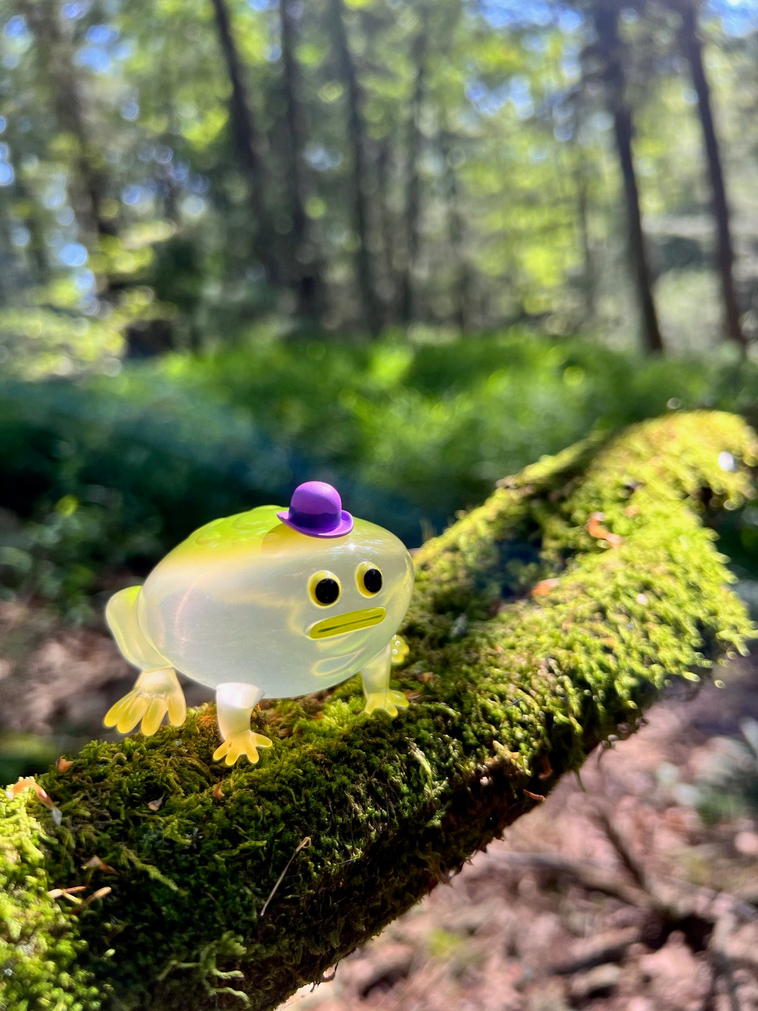 Green Glass Frod by Sad Salesman, a small resin toy frog perched on a branch, wearing one of five interchangeable PVC hats.