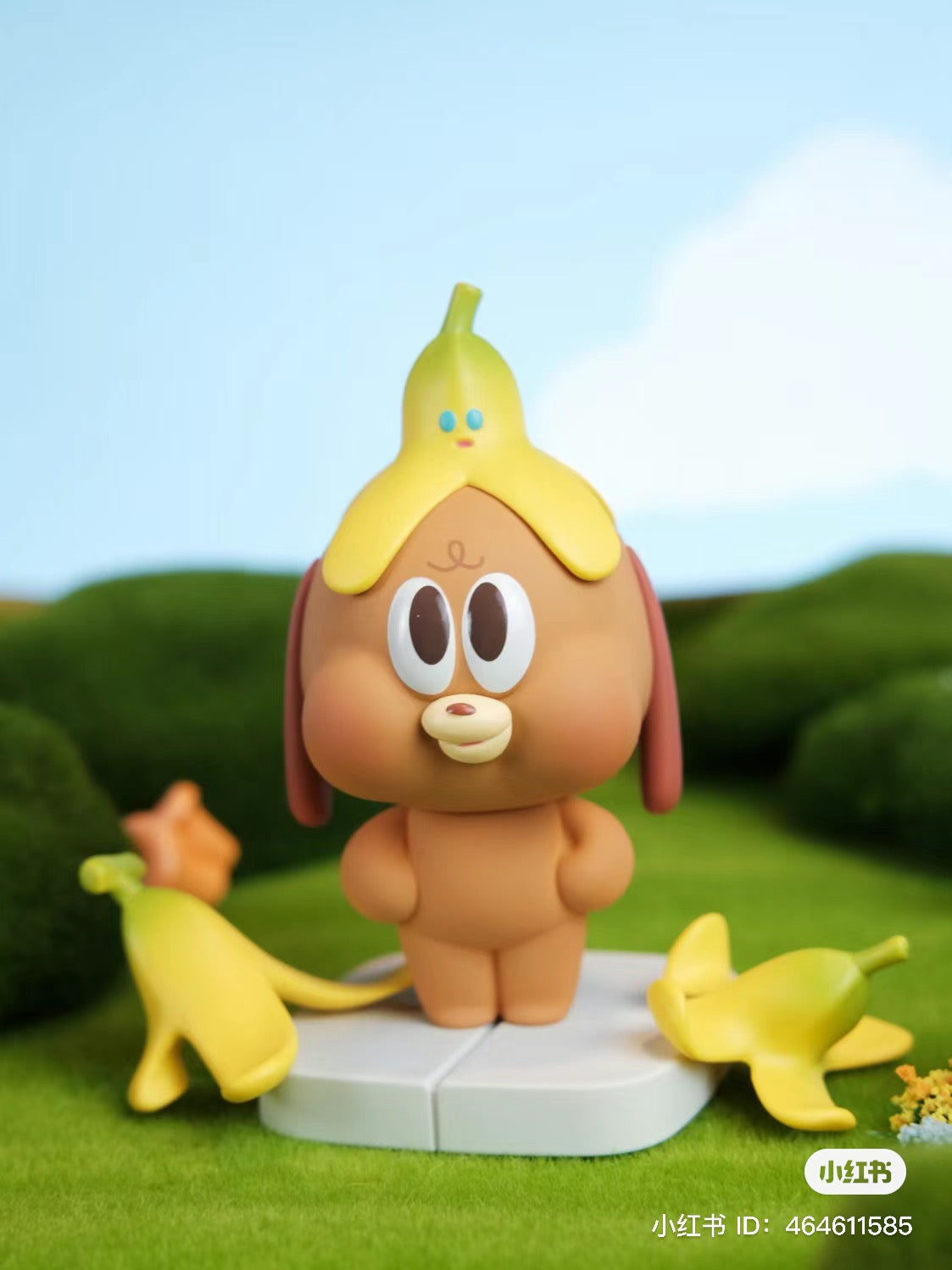 A cartoon animal figurine from the HAPPY & COCKY Blind Box Series with a banana on its head, surrounded by toys and grass. Preorder now from Strangecat Toys.