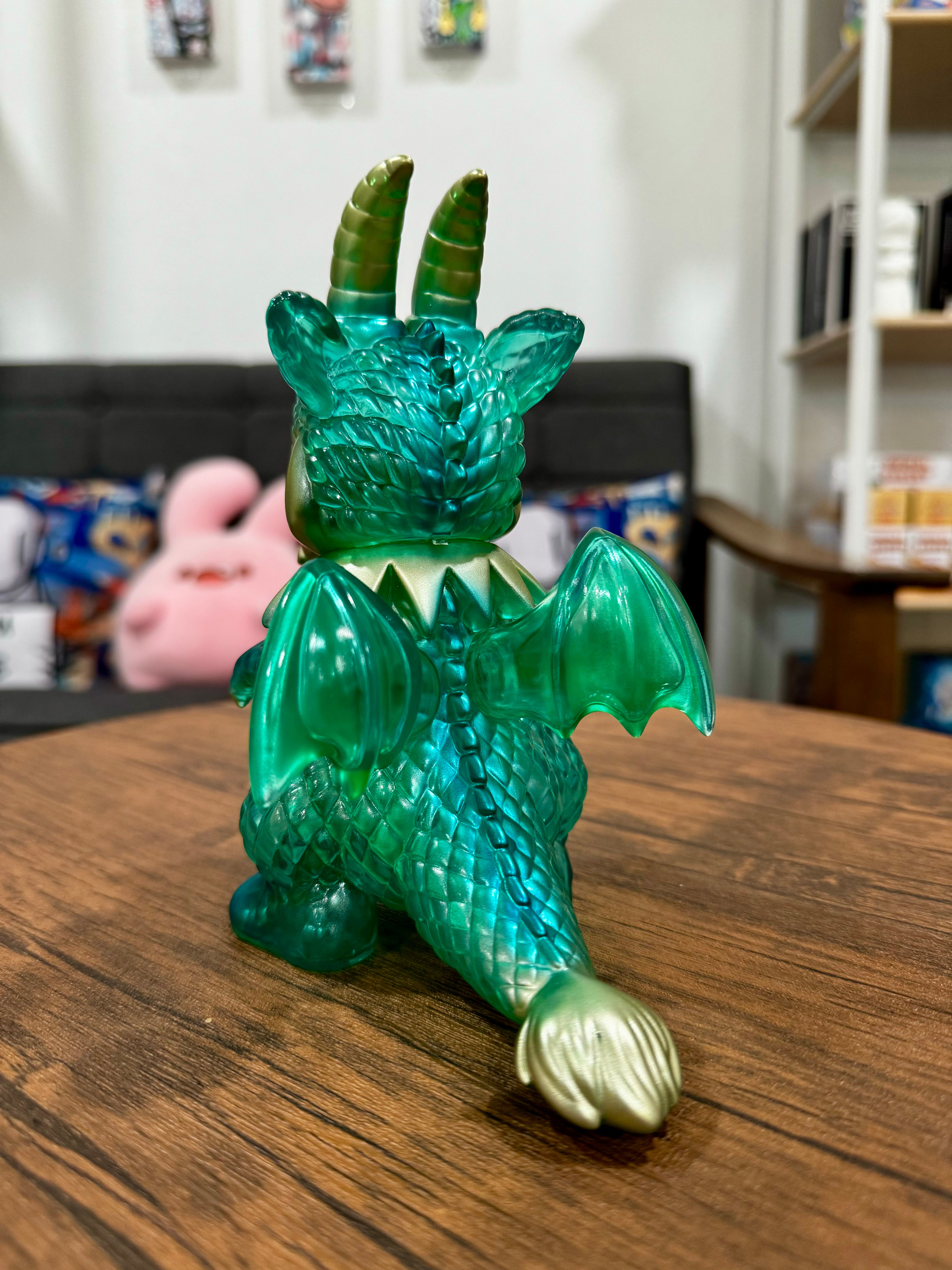A green dragon toy figurine named Calm Dragon Clear Mint by Art Junkie on a wooden surface. From Strangecat Toys, a blind box and art toy store.