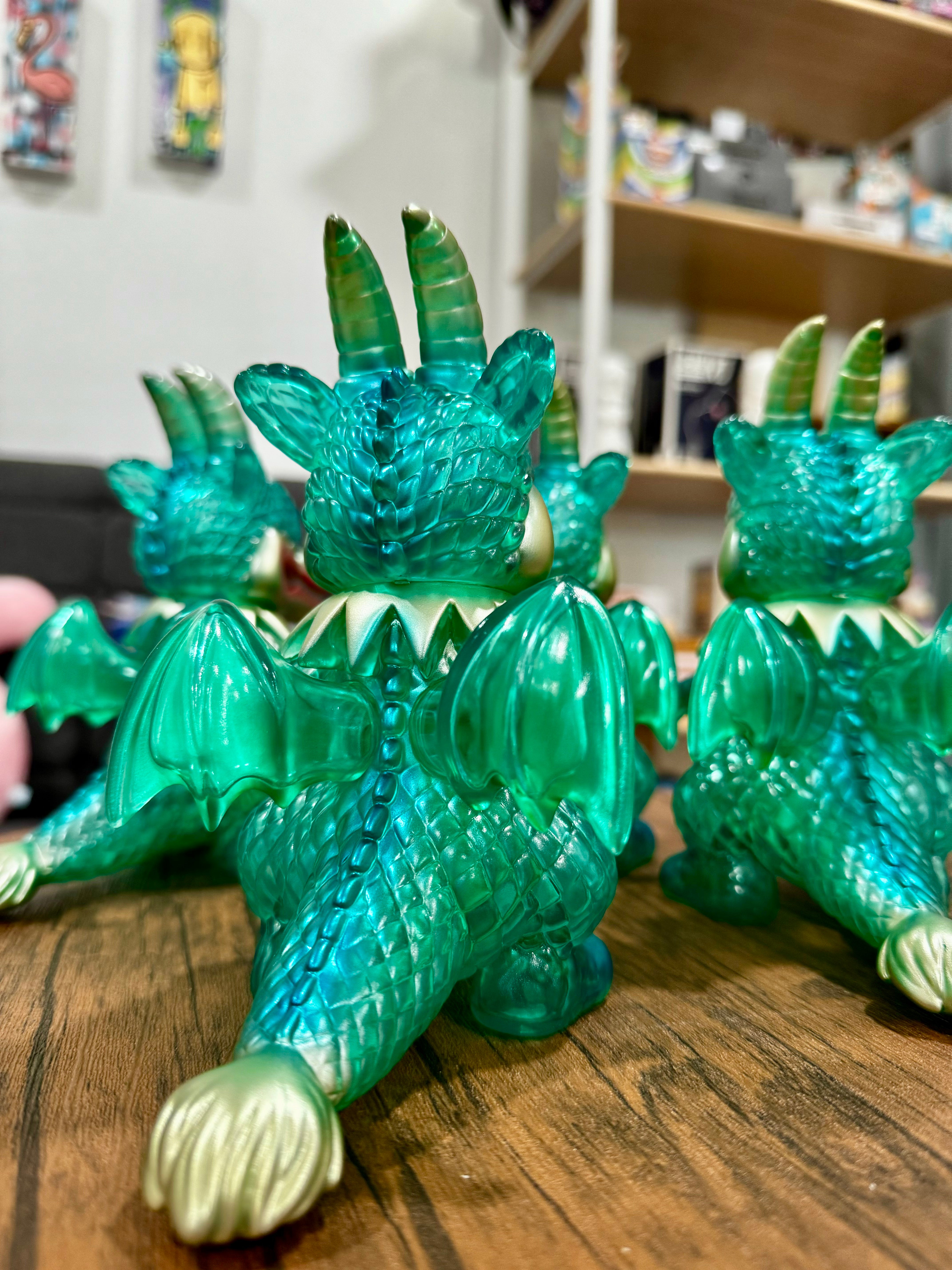 A group of green plastic dragon figurines, including a close-up of the Calm Dragon Clear Mint toy by Art Junkie, embodying Strangecat Toys' blind box and art toy store essence.