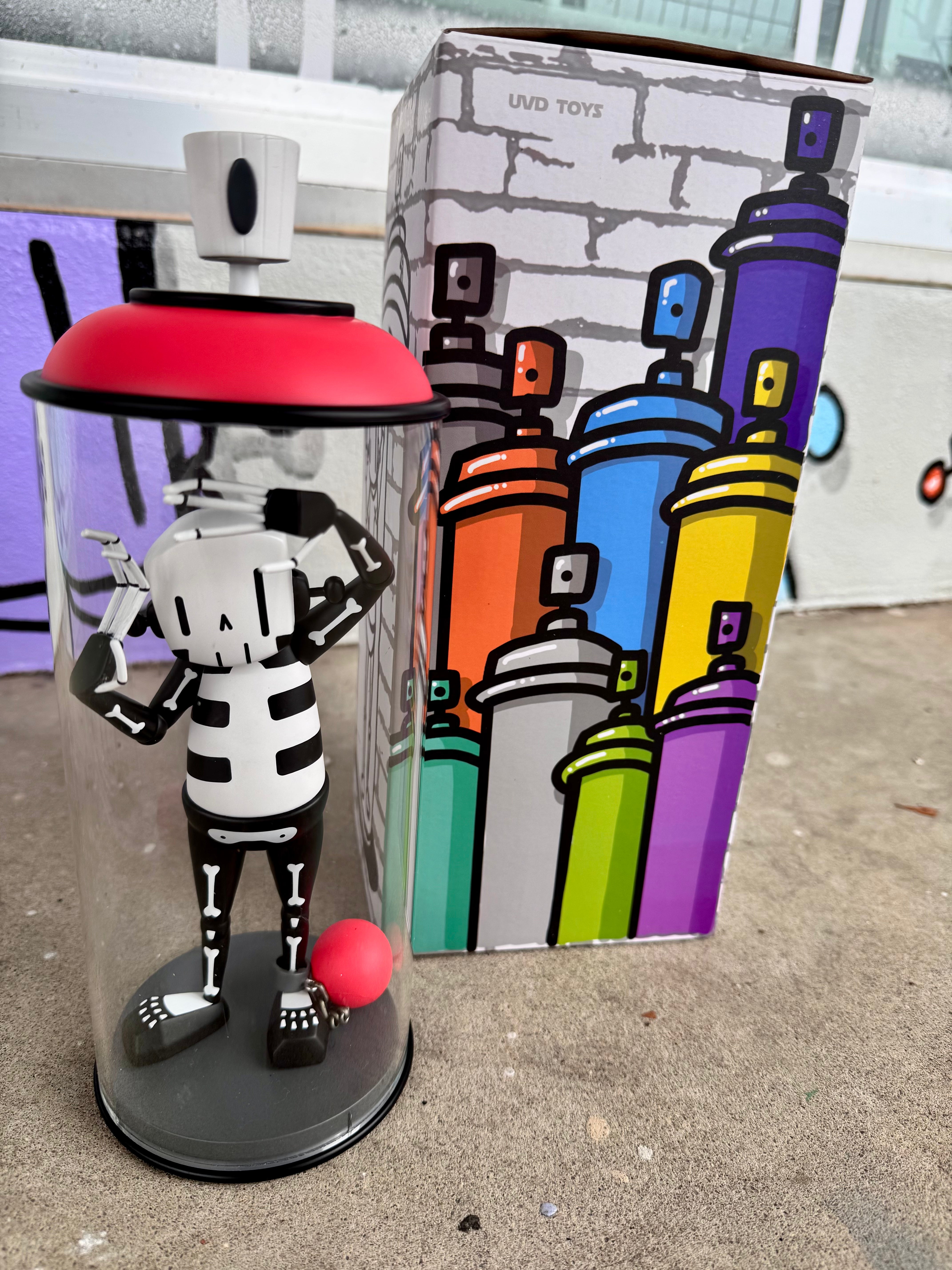 Contents Under Pressure Vinyl Figure - Bones Edition by Chris RWK in packaging, featuring a stylized skeleton in an acrylic spray-can display with toy ball-and-chain, produced by UVD Toys.