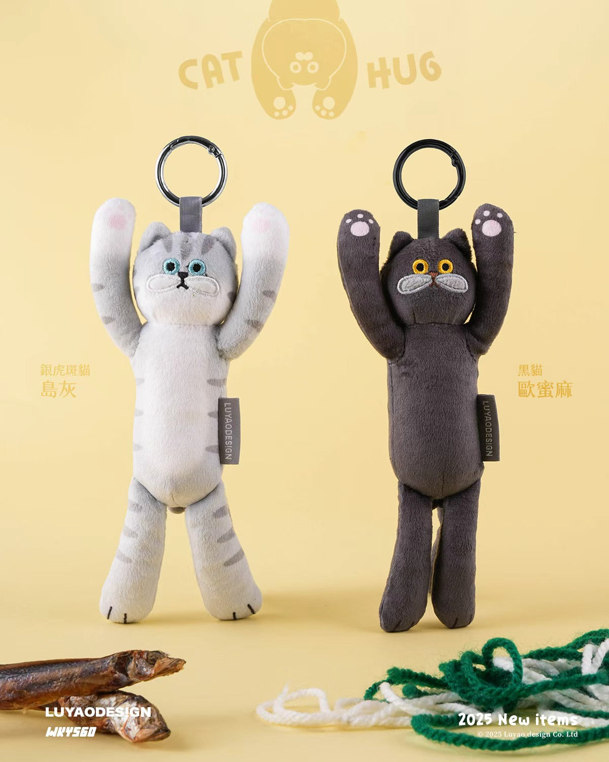 Two Cat Hug plush key-chains, one light gray, one dark charcoal, with raised arms and embroidered paws, against a playful background with yarn and treats.