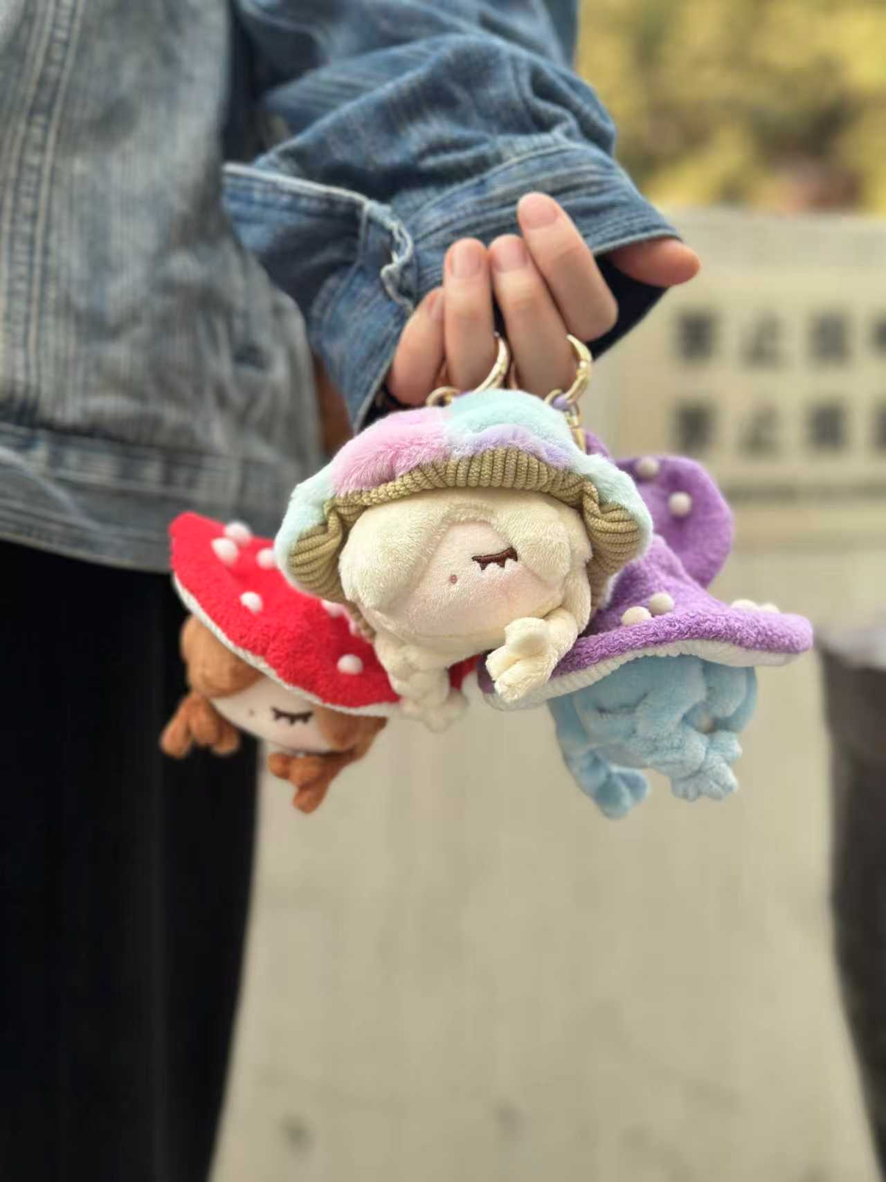 Hand holding three Little Mushroom Plush Pendant keychains, featuring sleeping girl designs with varied mushroom caps, part of a six-design blind box series.