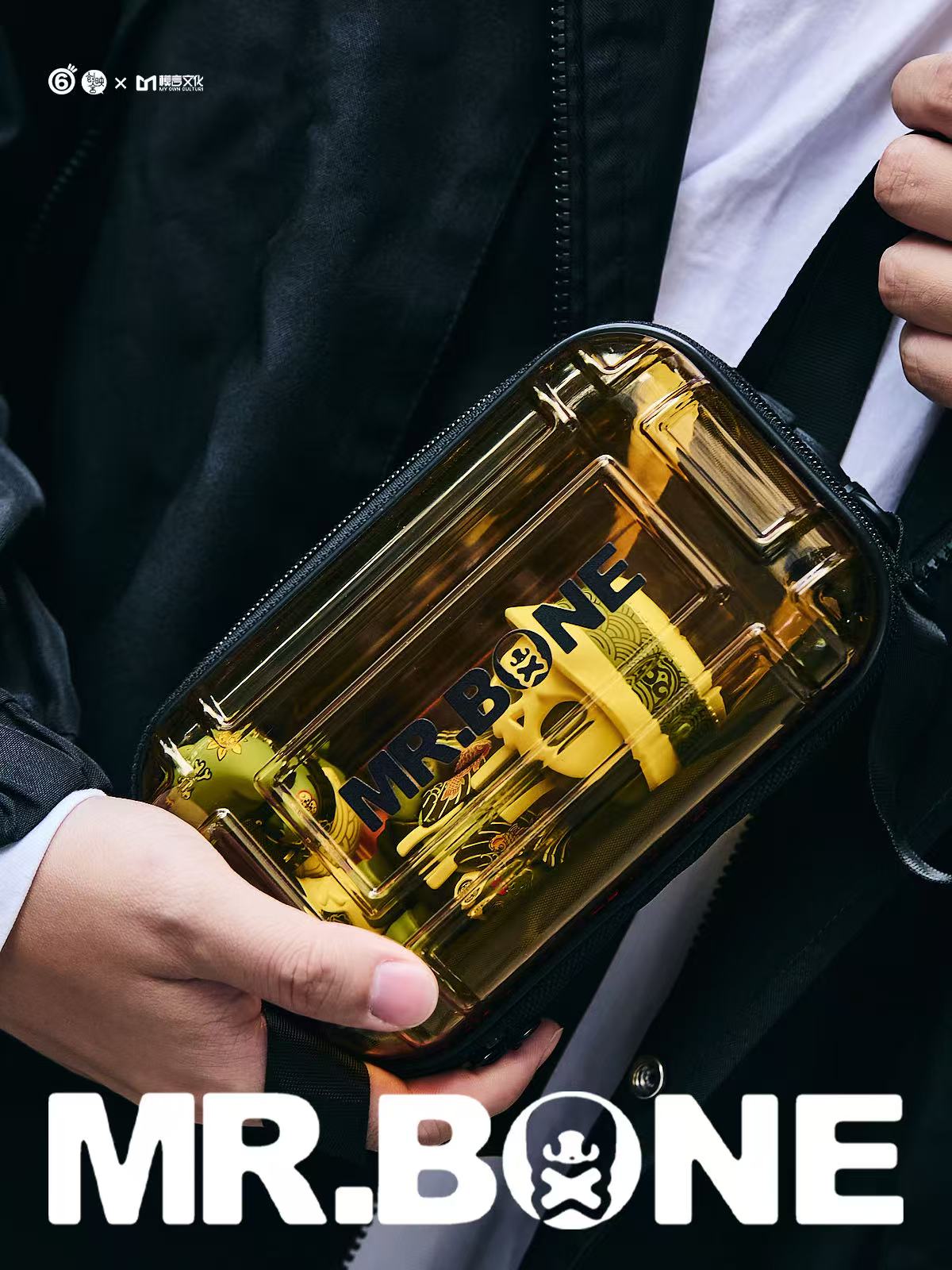Mr Bone Yakuza Limited Set 100% - Preorder: Transparent yellow pouch with MR.BONE logo, showcasing branded items inside, held by a person in a black jacket.