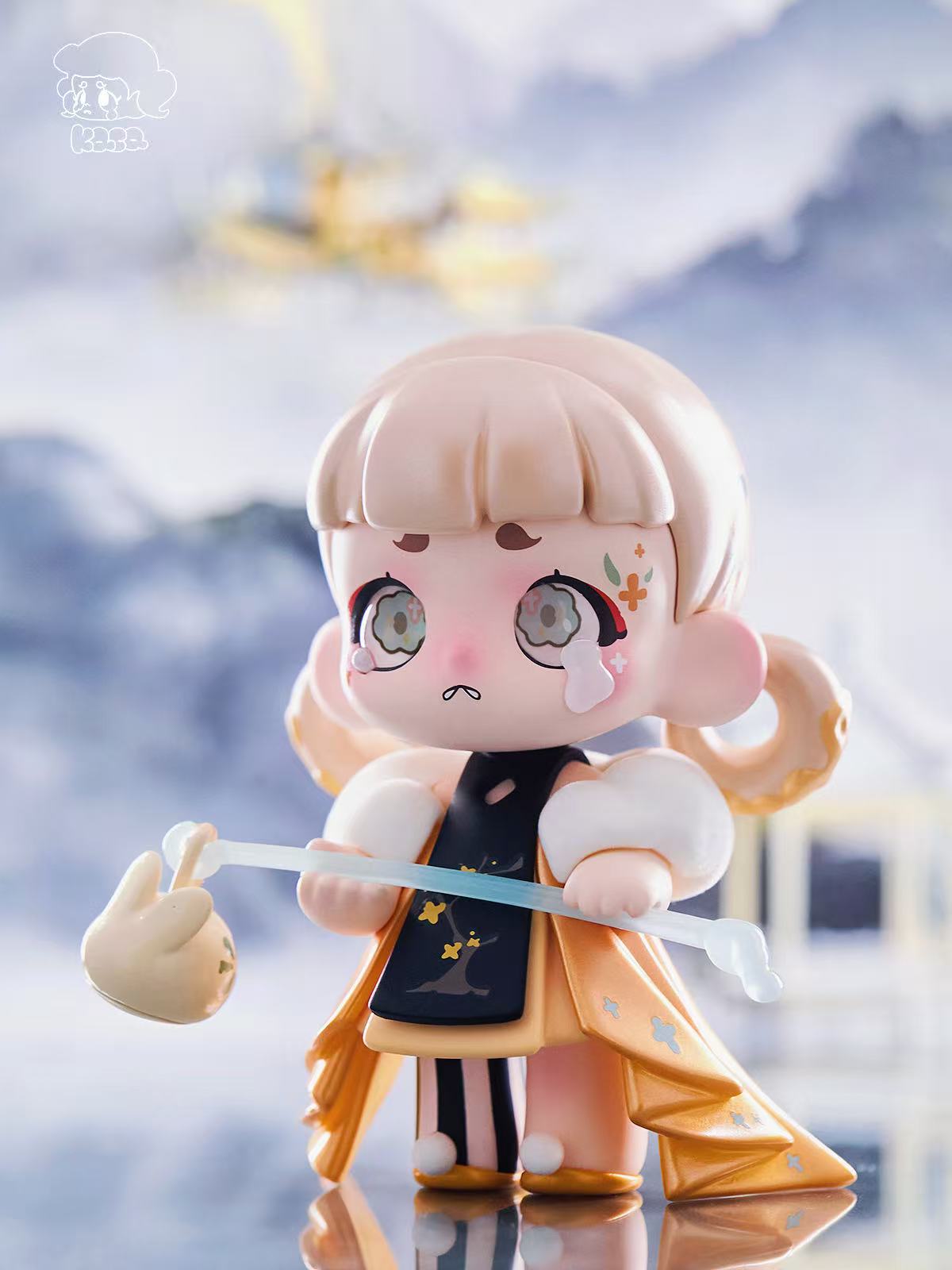 KASA 2.0 - Mystic Tales Blind Box Series figure with large head, side buns, expressive eyes, golden-orange coat, and translucent staff, set in a dreamy, wintry scene.