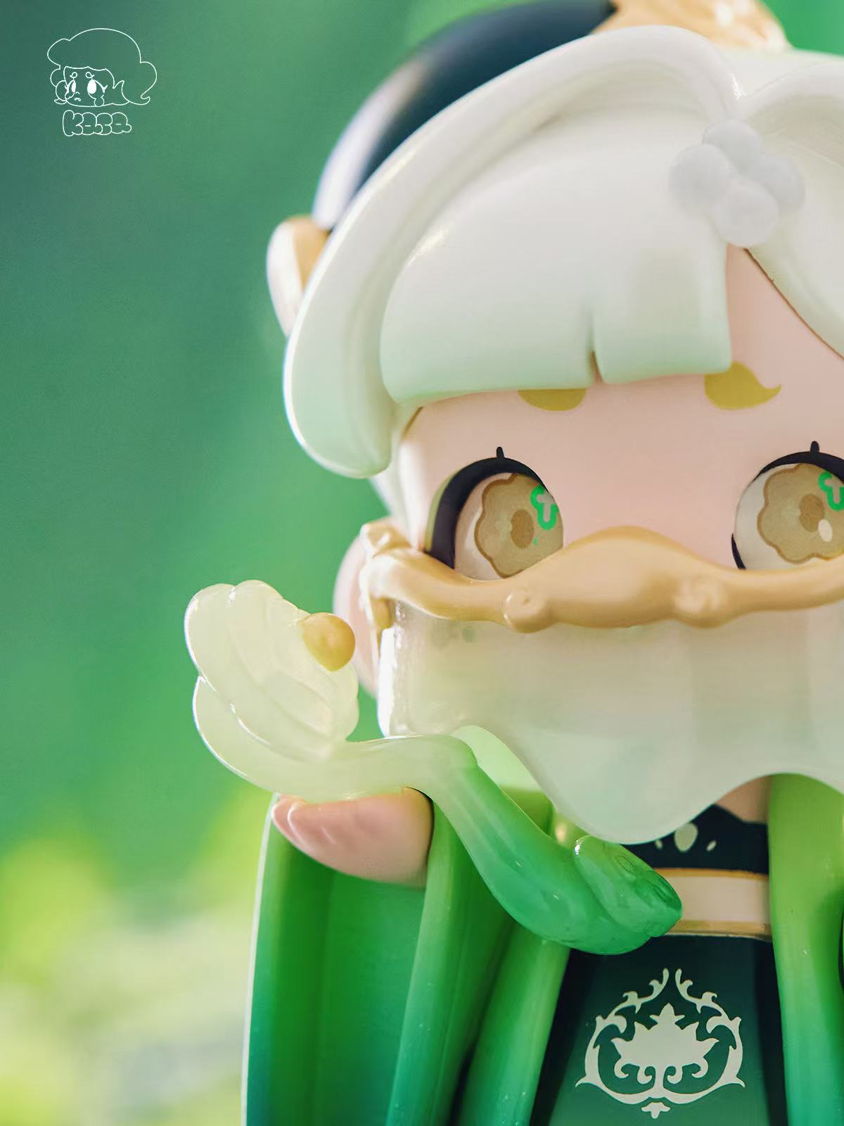 KASA 2.0 - Mystic Tales Blind Box Series figure with cookie-shaped eyes, a dripping-glaze mask, green cloak, and translucent green wand against a soft background.