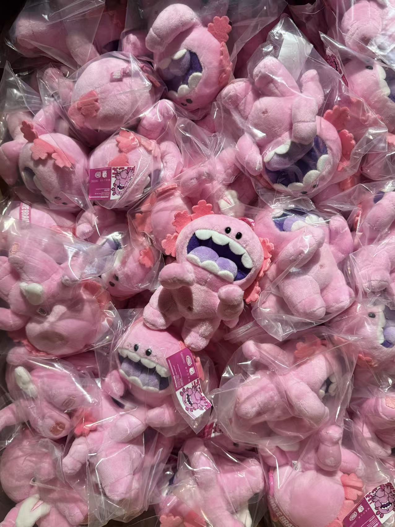 Macaroni plush doll keychain by Grape Brain, featuring pink axolotl-like creatures with frilly gills and toothy smiles, individually wrapped, available for preorder.