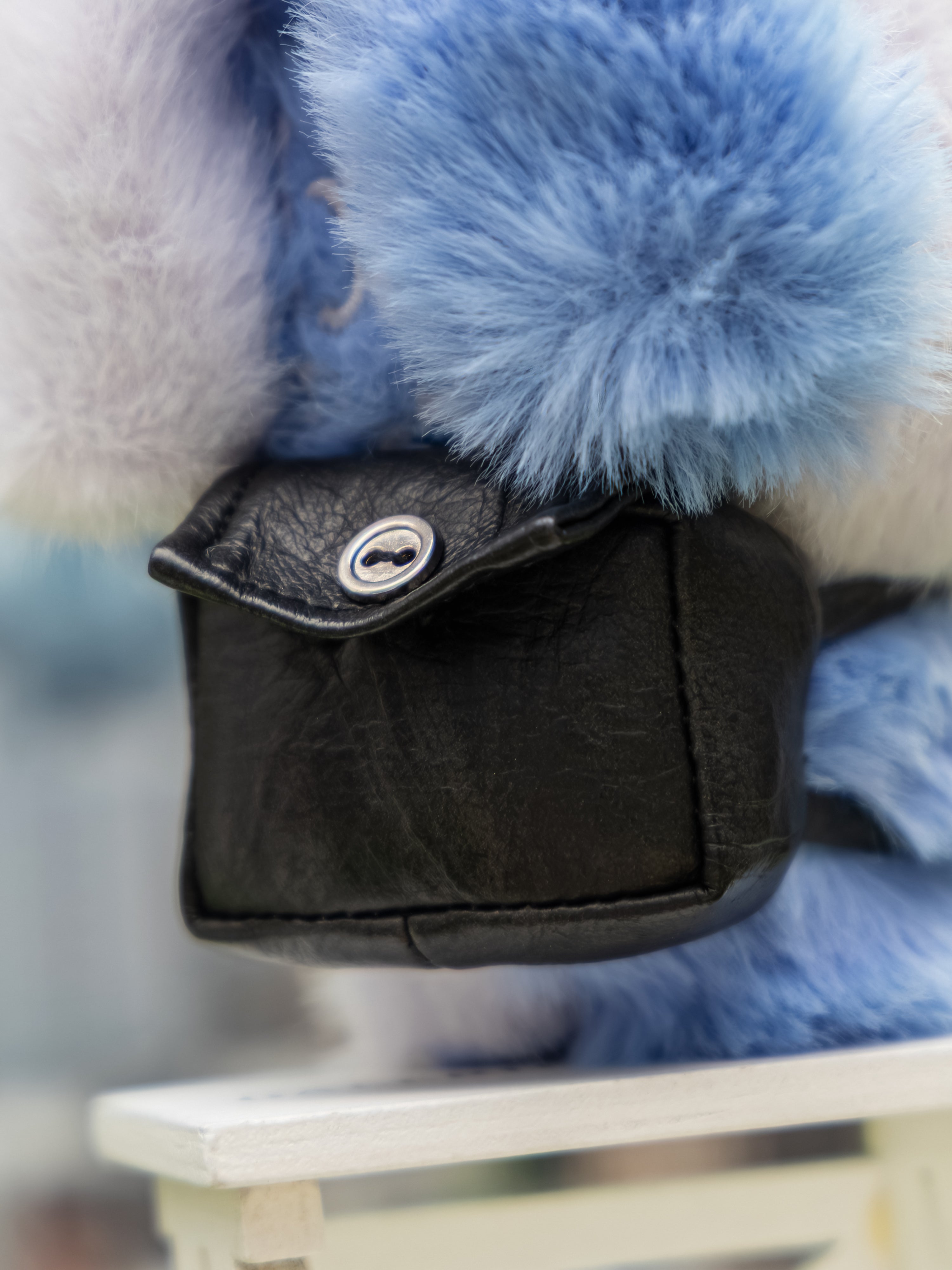 Close-up of Q. Kid Outdoor Activities Series PVC Plush Blind Box, featuring a small black leather bag with a silver-tone snap, set on faux-fur.