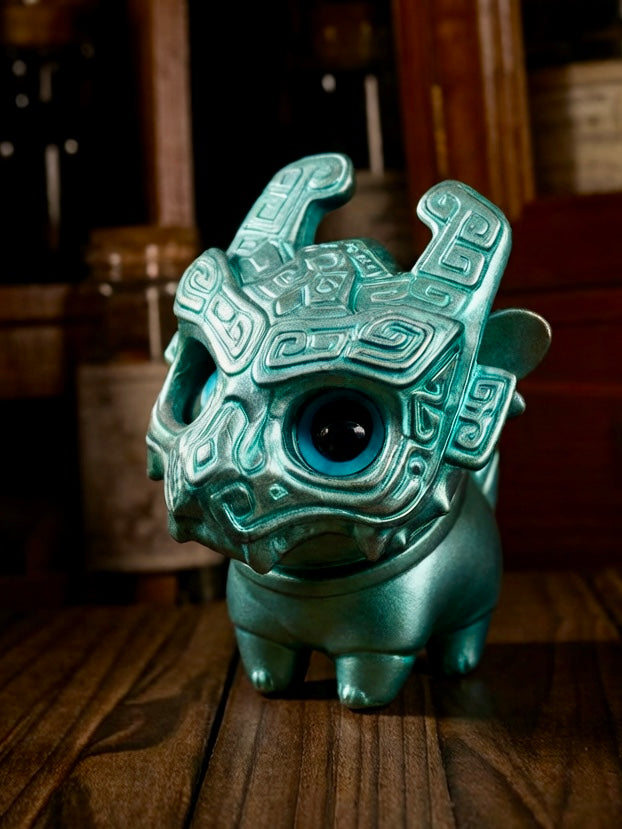 Little Bronze Taotie by HOTRU, a metallic teal-green collectible toy, features a rotatable head and removable dragon mask, posed on a tabletop. Preorder available.