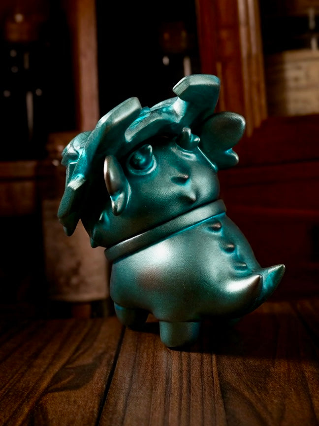 Little Bronze Taotie by HOTRU - Preorder; a metallic teal figurine with a petal crest, cartoon eyes, tiny arms, on a wooden surface.