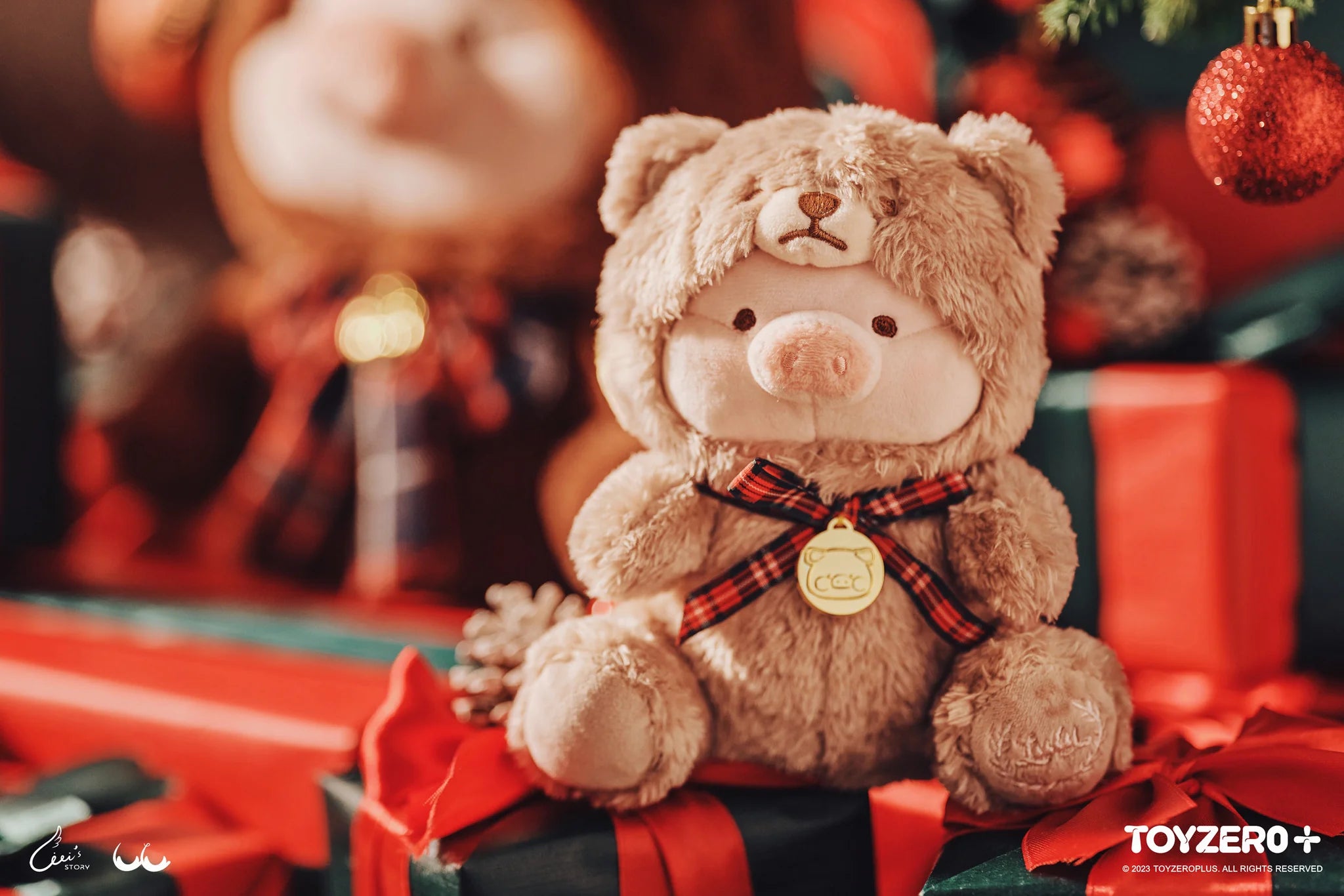 LuLu the Piggy plush teddy bear sitting on a present with a gold tag and a piggy coin medal.