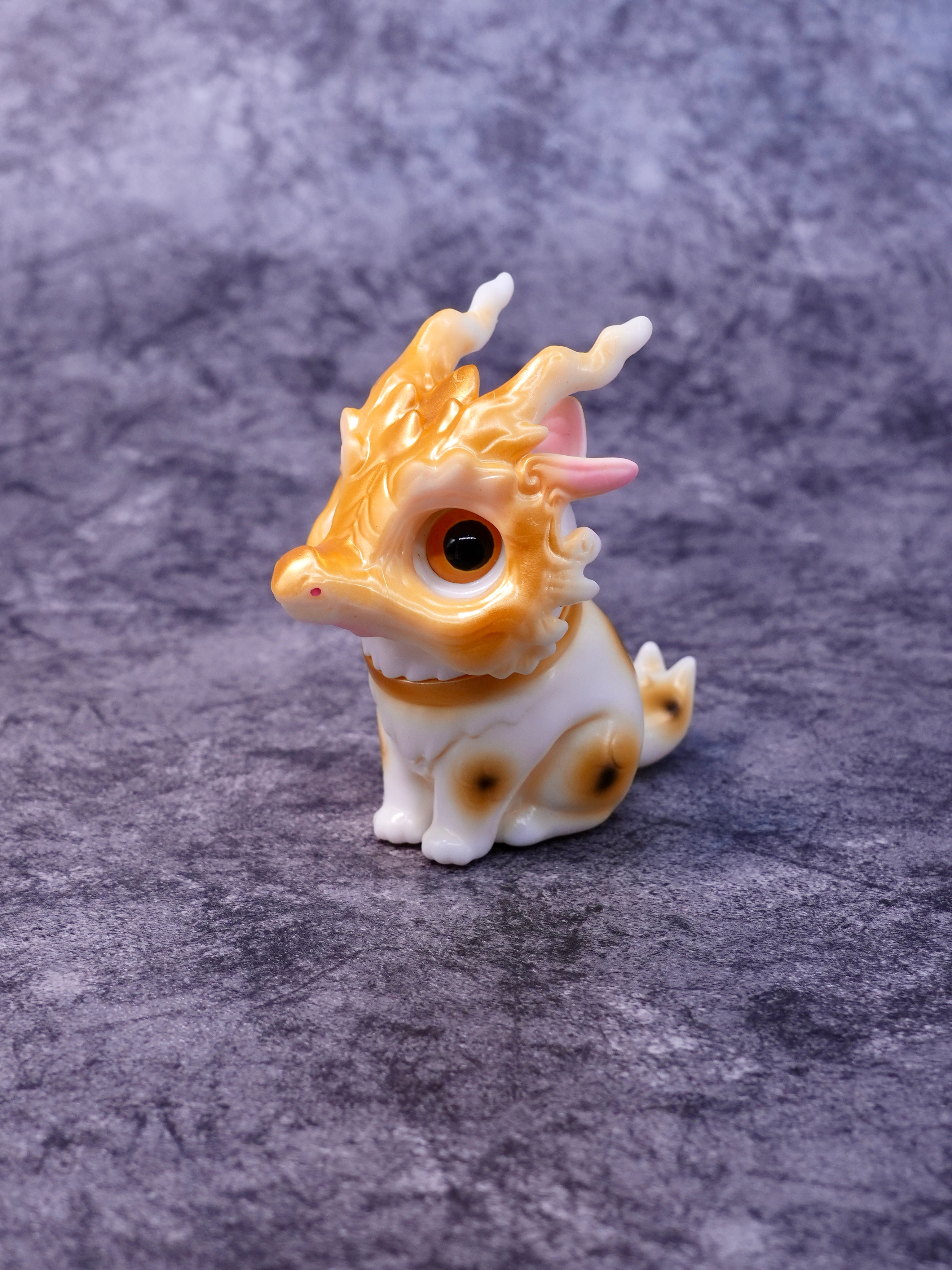 Lucky Loong cat by HOTRU - Preorder. A glossy white vinyl figurine of a dragon-cat with a rotatable head and amber accents, holding a dragon bone mask.