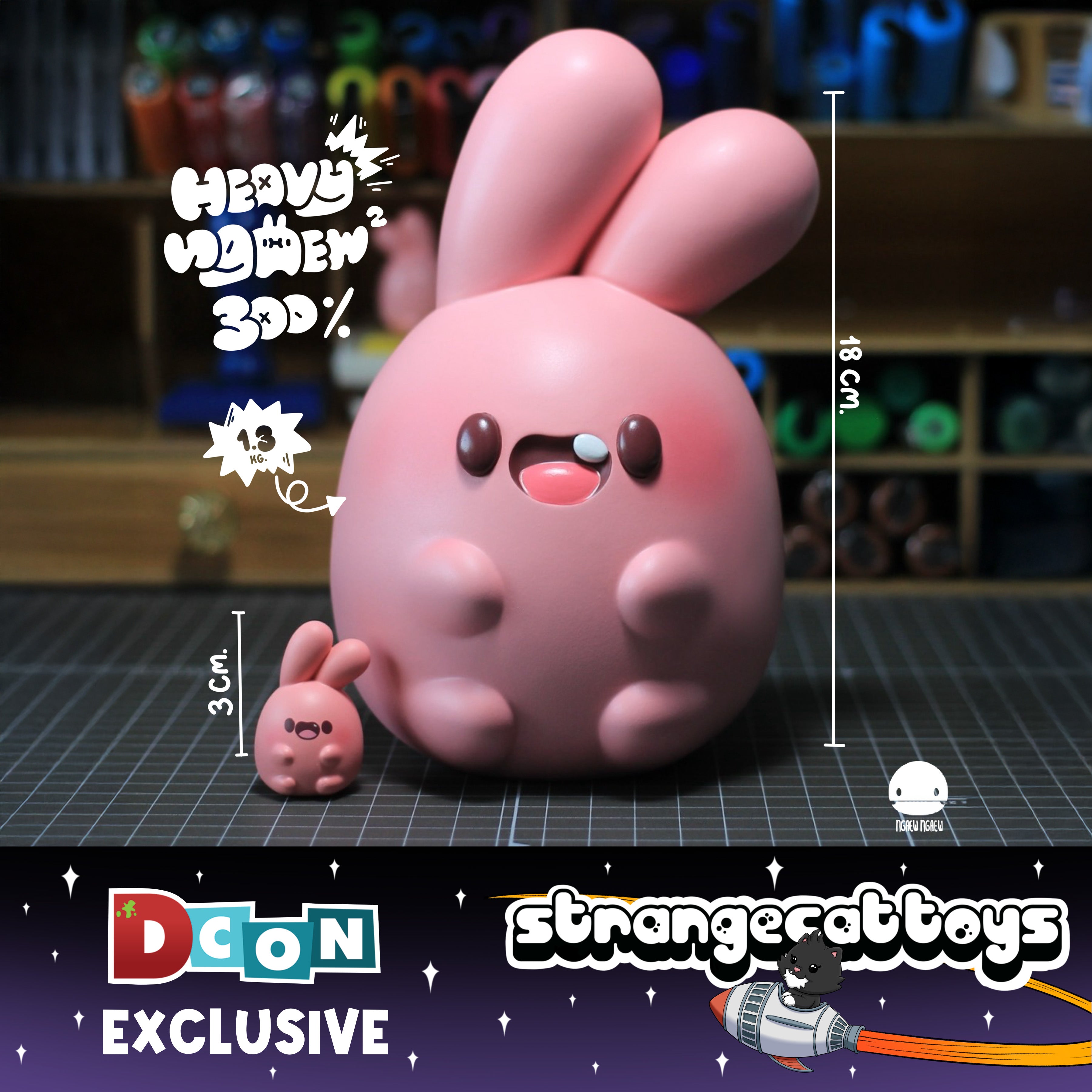 Two vinyl figures, NGAEW Heavy by Ngaew Ngaew: 18cm tall, 1.3kg large bunny, and 3cm miniature. DCon Exclusive from Strangecat Toys, featuring cat-astronaut logo.