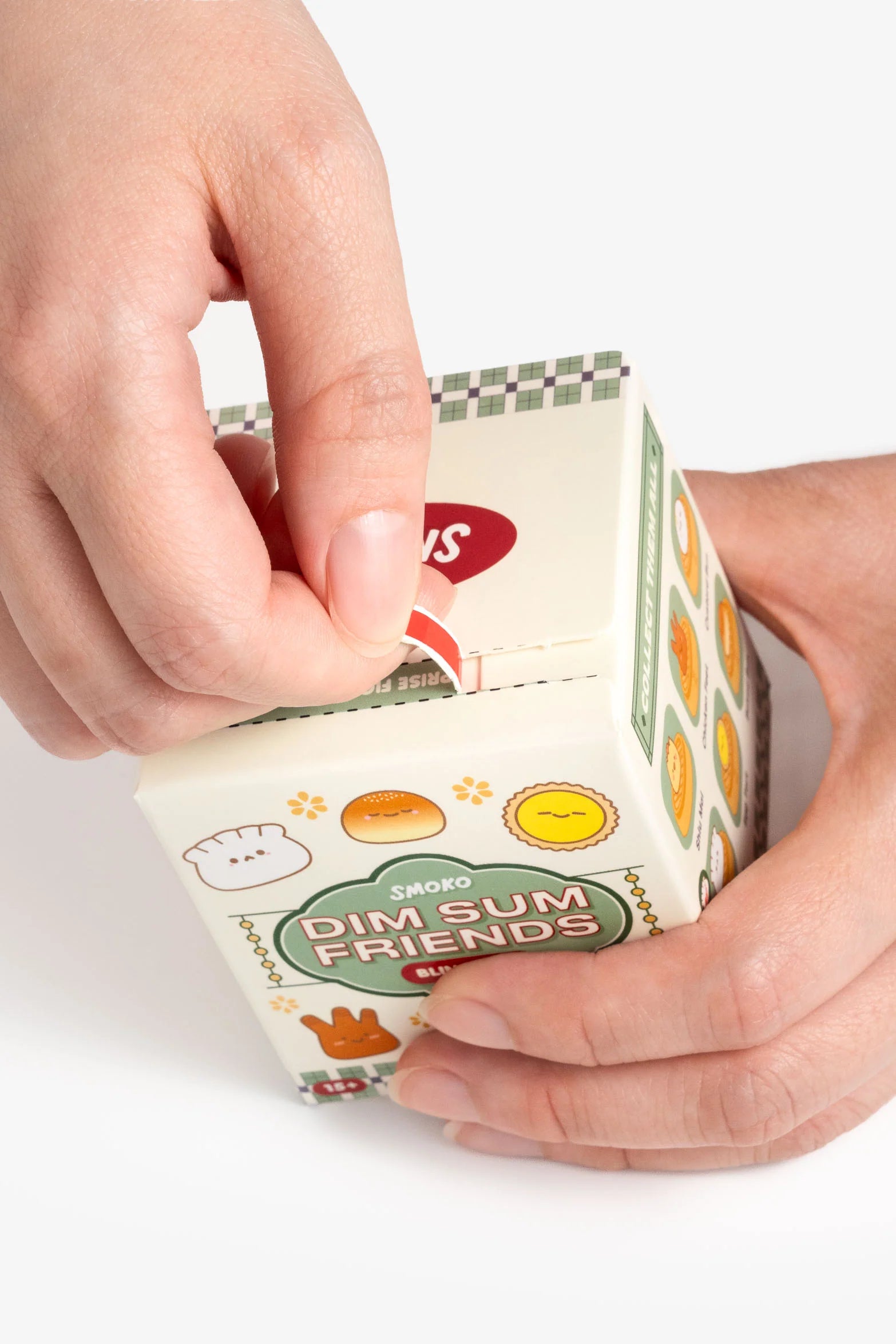 Hands opening a Smoko Dim Sum Friends Blind Box Figure, featuring smiling dumpling illustrations and a pull-tab seal, revealing a surprise collectible miniature inside.