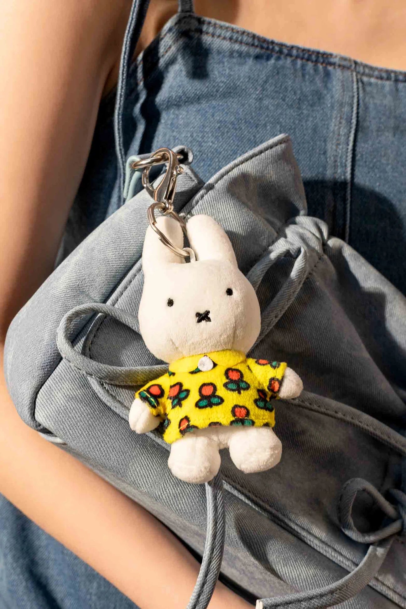 Smoko Miffy Tulip Bag Charm: a small white plush-bunny keychain in a floral yellow top, clipped to a light-wash denim bag.