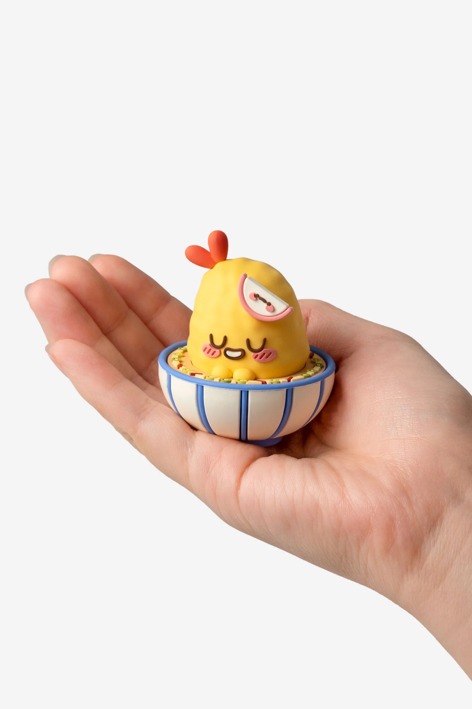 Hand holding a Smoko Tempura Shrimpie Blind Box Figure, featuring a yellow chick lounging in a striped bowl with a semicircular garnish, collectible from Strangecat Toys.