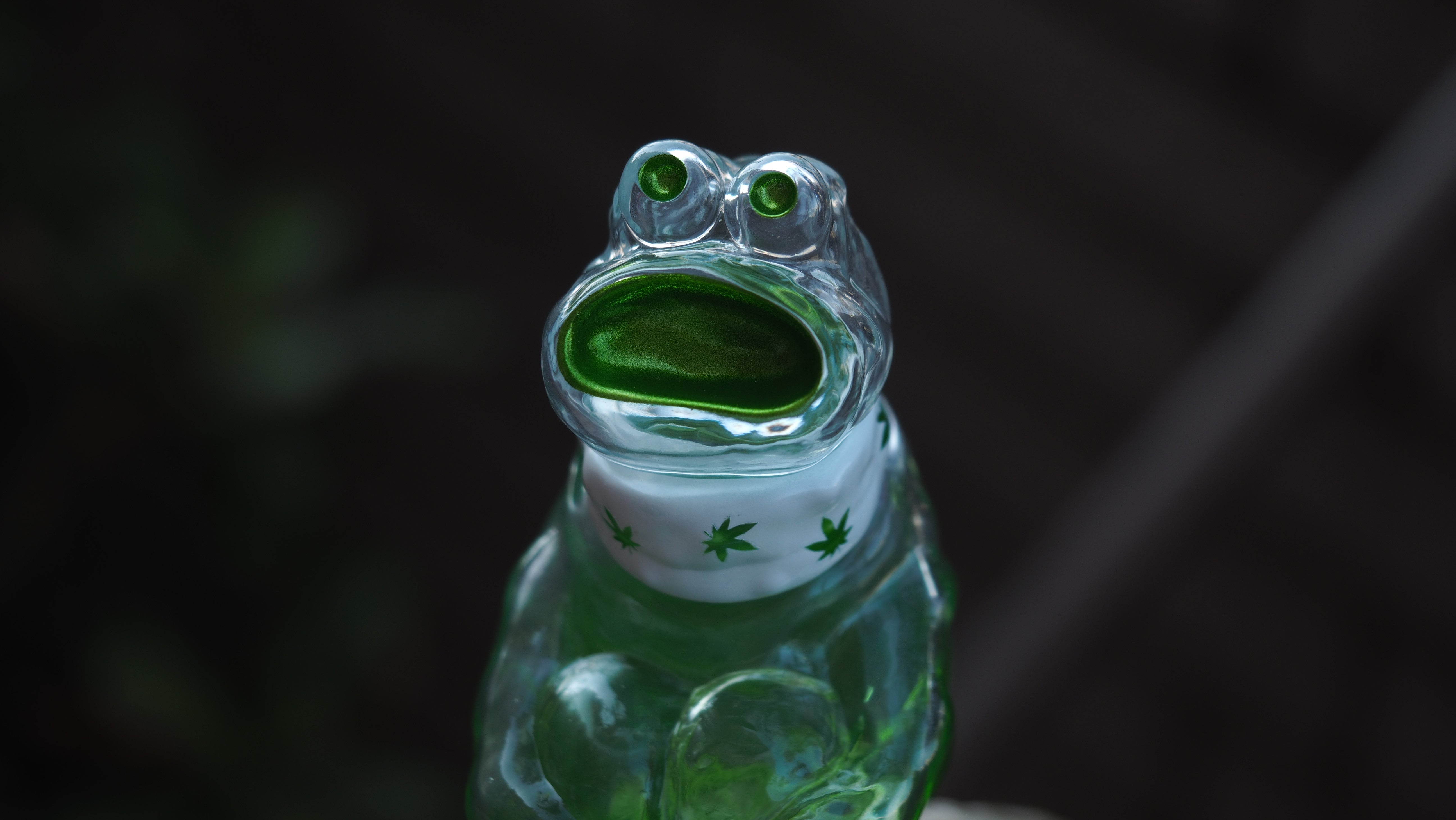 A glass frog figurine named BONG A-MON, 9 cm tall, made of sofubi/resin, with green liquid and leaf design. Preorder - Ships Late May 2024.