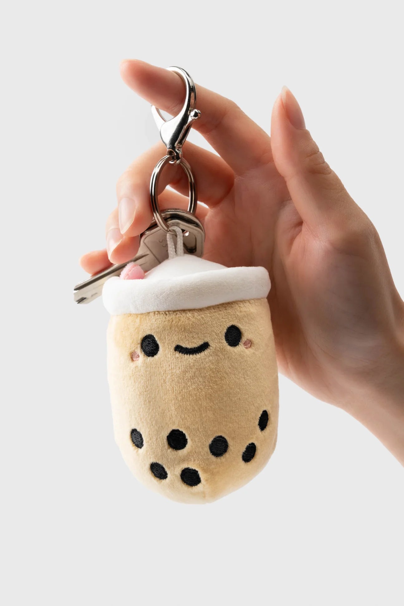 Hand holding Pearl Boba Tea Bag Charm, a plush bubble tea keyring with a smiling face, rosy cheeks, and black tapioca pearl details.