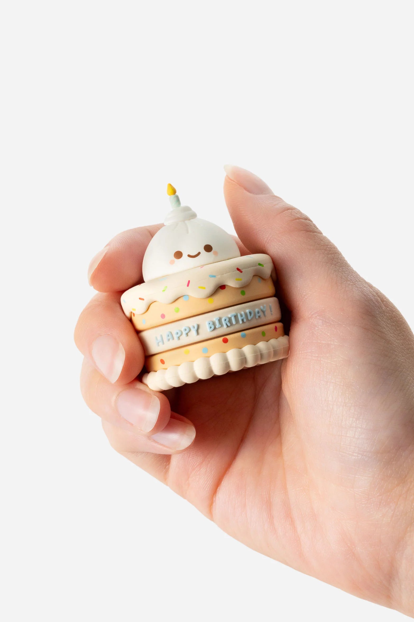 Person holding a kawaii-style Smoko Friends Birthday Cake Blind Box Figure, featuring pastel layers, rainbow sprinkles, a smiling face, and a HAPPY BIRTHDAY! message.