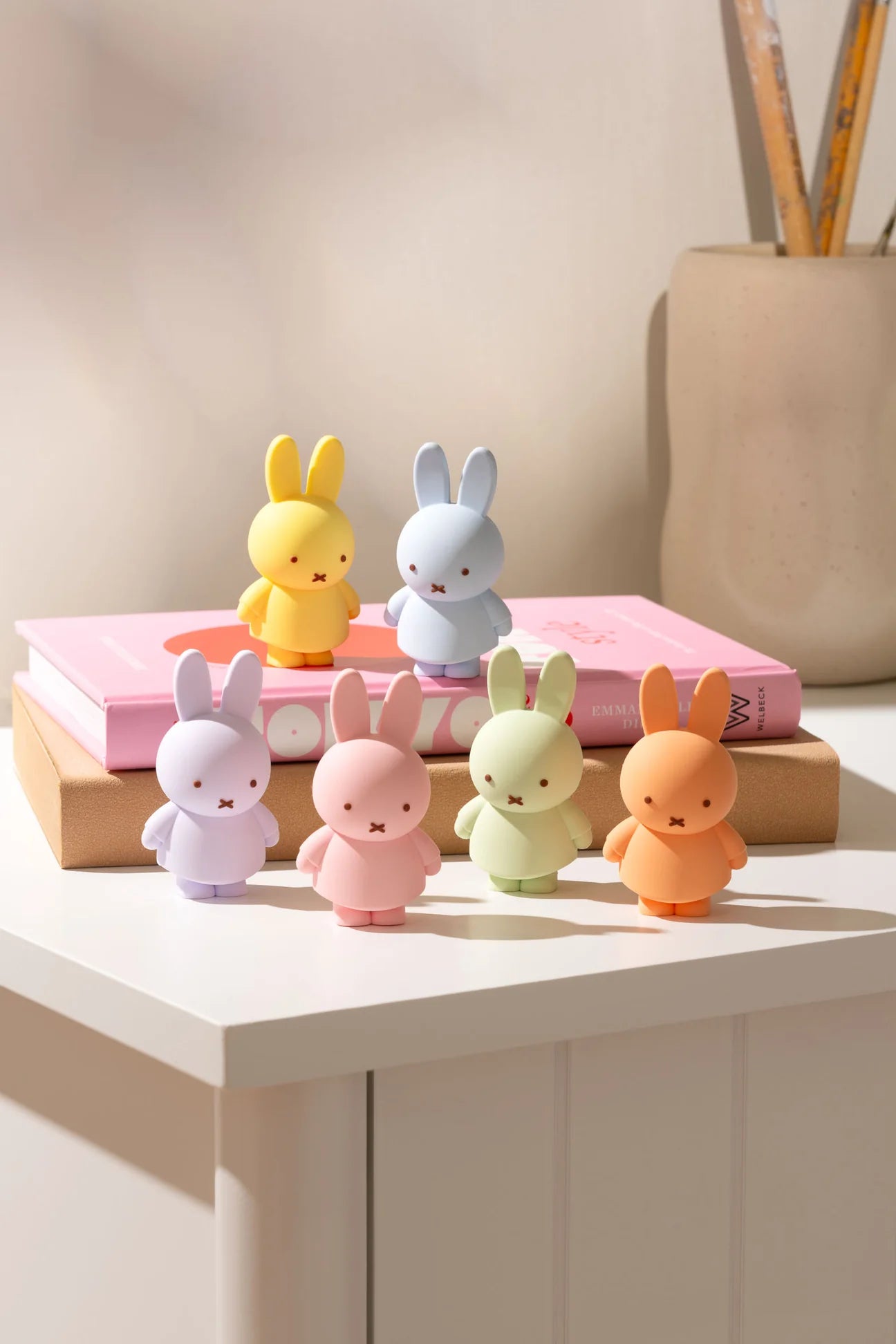Smoko Miffy Goes Pastel Blind Box Figures arranged on books, showcasing collectible vinyl rabbit figurines in pastel colors, perfect for art toy enthusiasts.