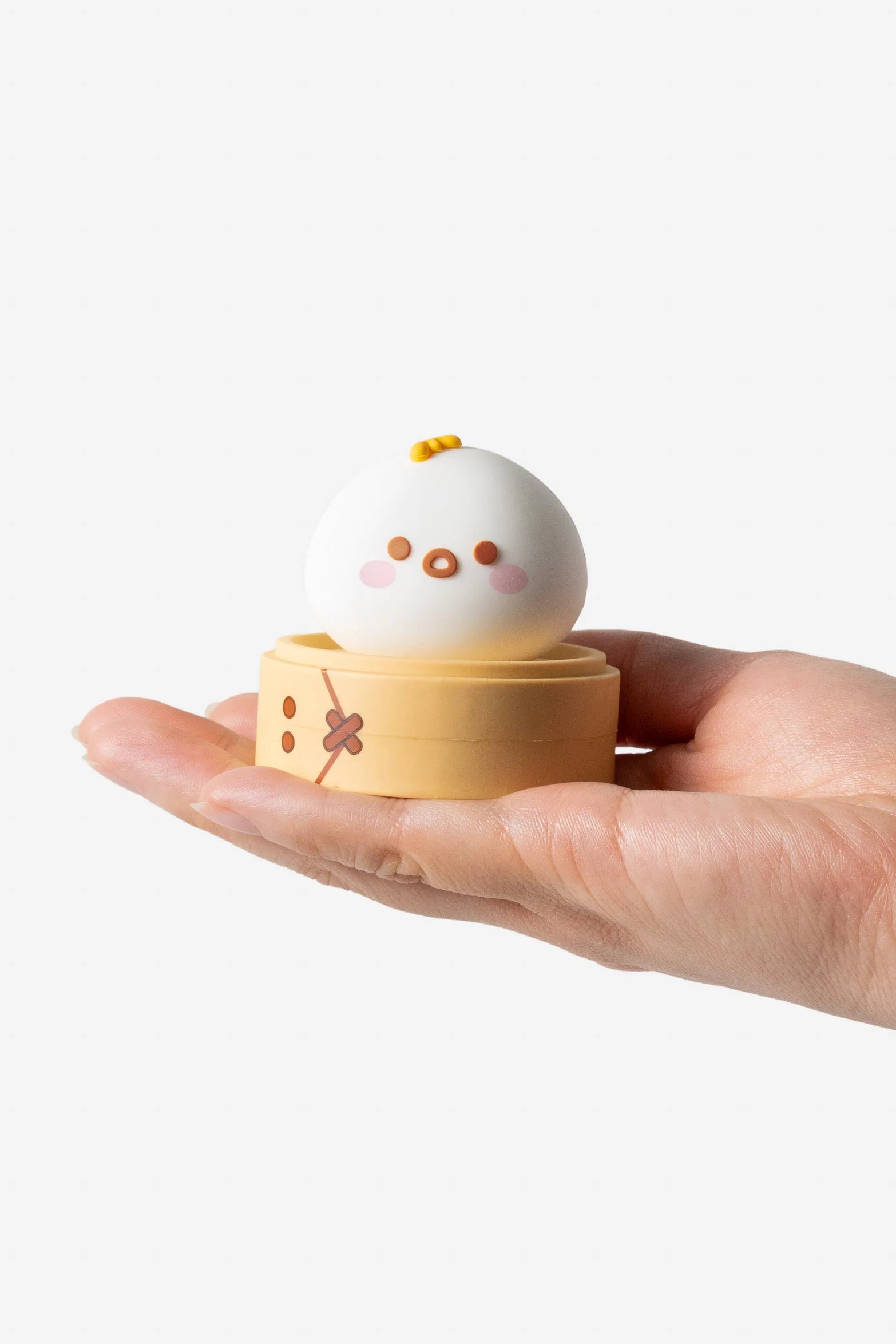 Hand holds Smoko Dim Sum Friends Blind Box Figure: a cute, white dumpling character with rosy cheeks in a bamboo steamer-style container, collectible vinyl toy.