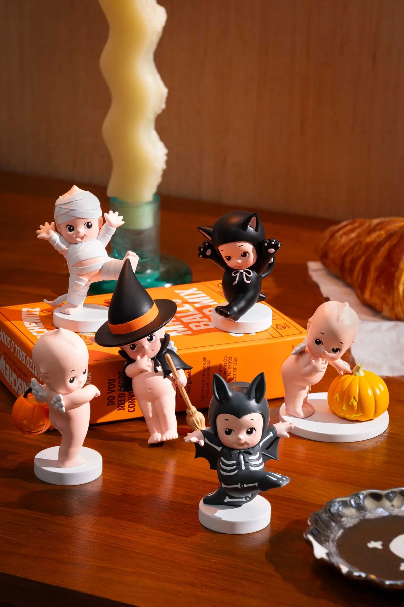 Smoko Kewpie Halloween Blind Box Figures in costumes, including a mummy and witch, displayed on stands. Features collectible vinyl figures, recommended for ages 15+.