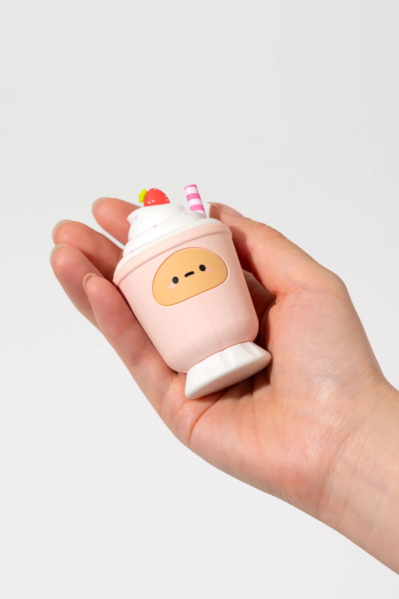 Hand holding Tayto's Diner Blind Box Figure, a kawaii-style squishy shaped like a pink milkshake with whipped cream, strawberry, and cartoon face.