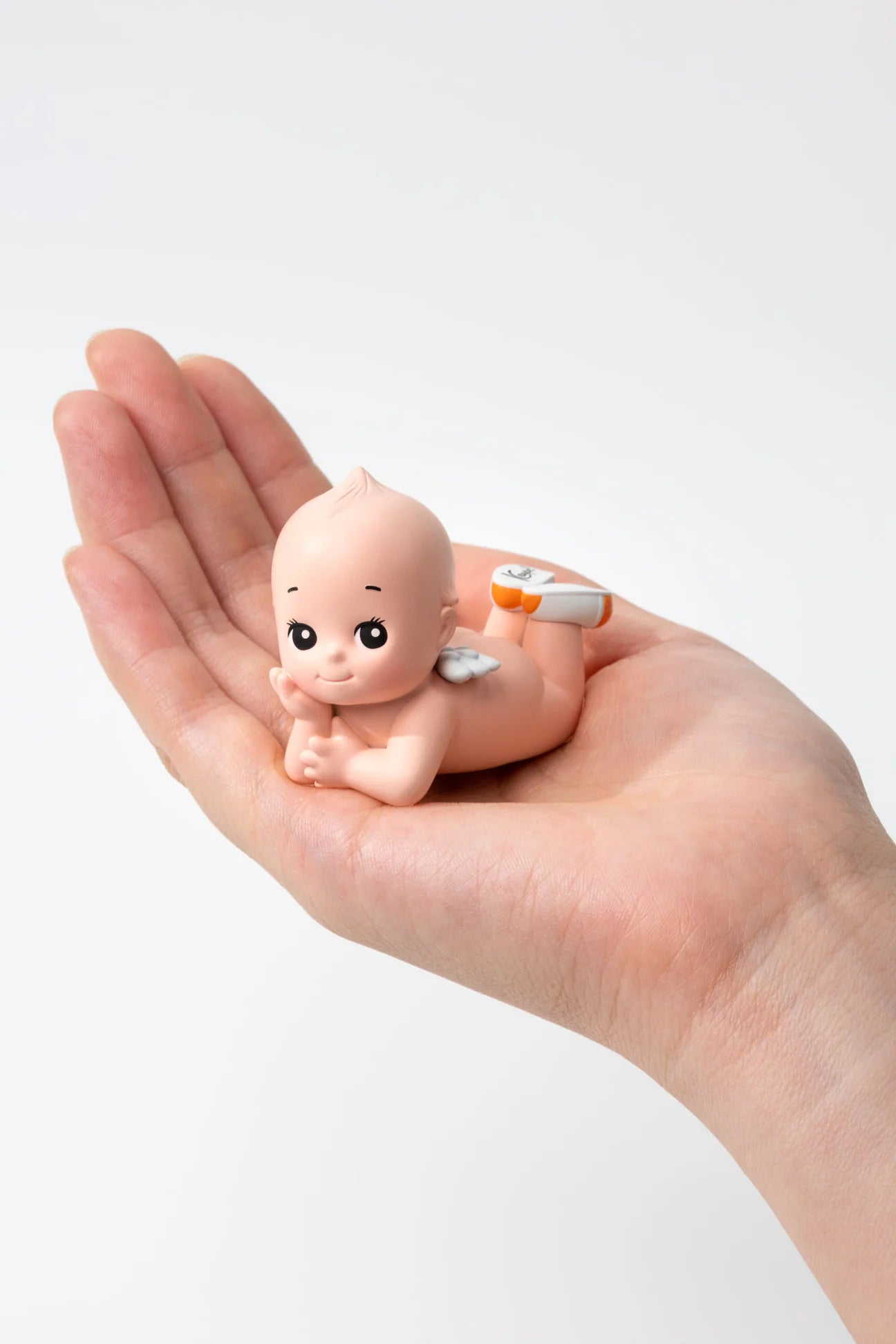 Smoko Kewpie®️ Blind Box Figure; cherub-like baby figurine with wings, lying on a palm, part of a collectible line by Kewpie Corporation.