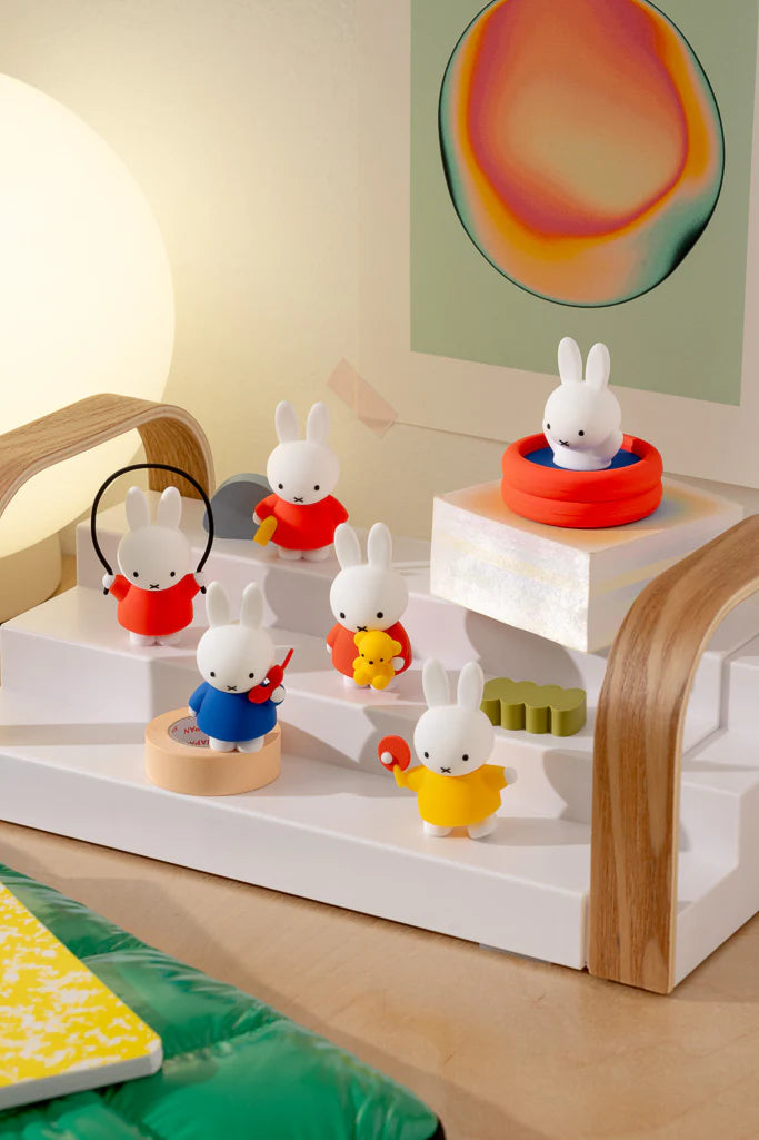 Miffy Doing Things Blind Box display featuring six Miffy figurines in various activities, each with unique props, arranged on a tiered platform.