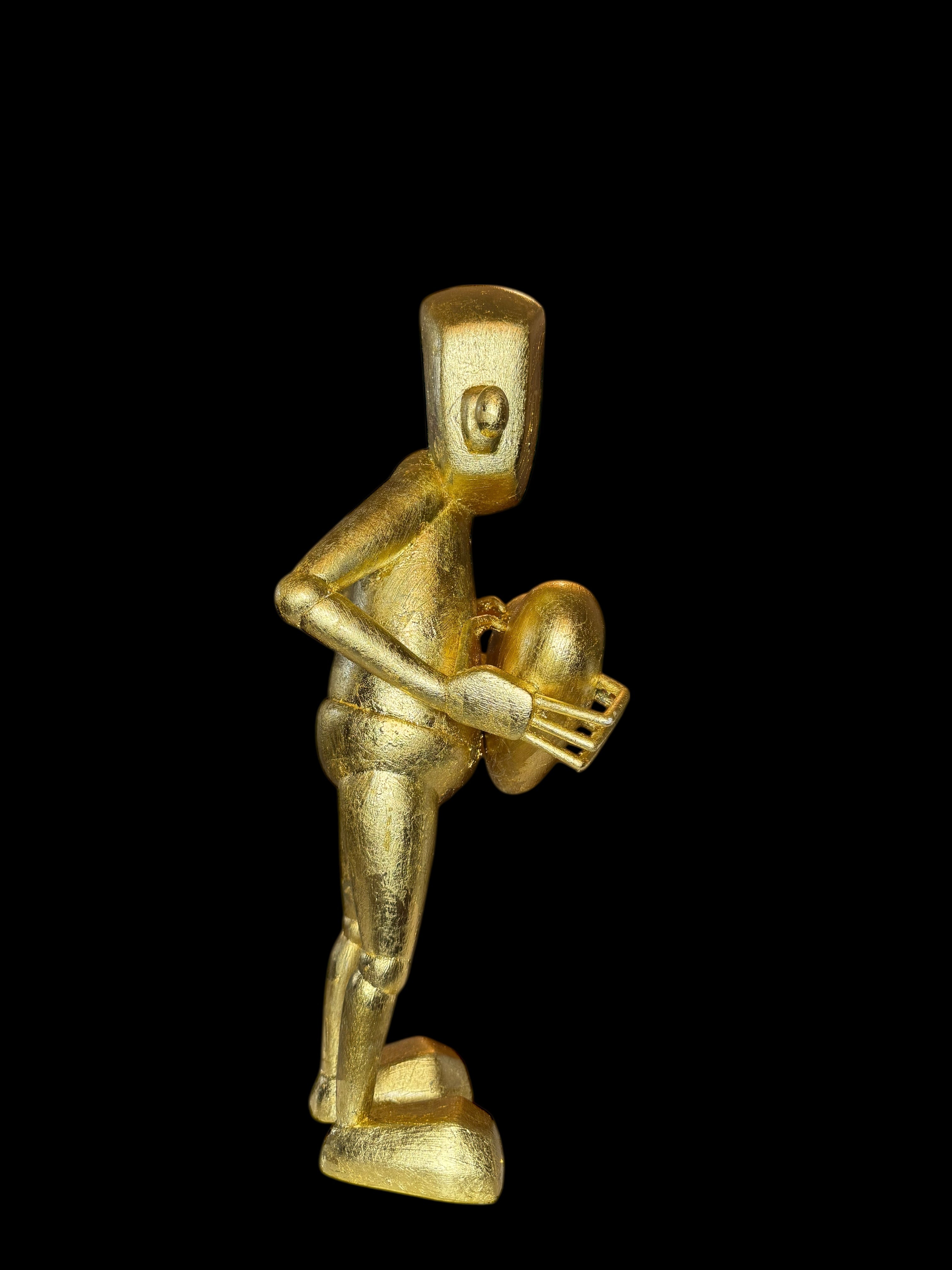 Time Will Tell - False idle by Chris RWK: A 15 metallic-gold figurine with block-headed design, holding an oval object, on a platform base.