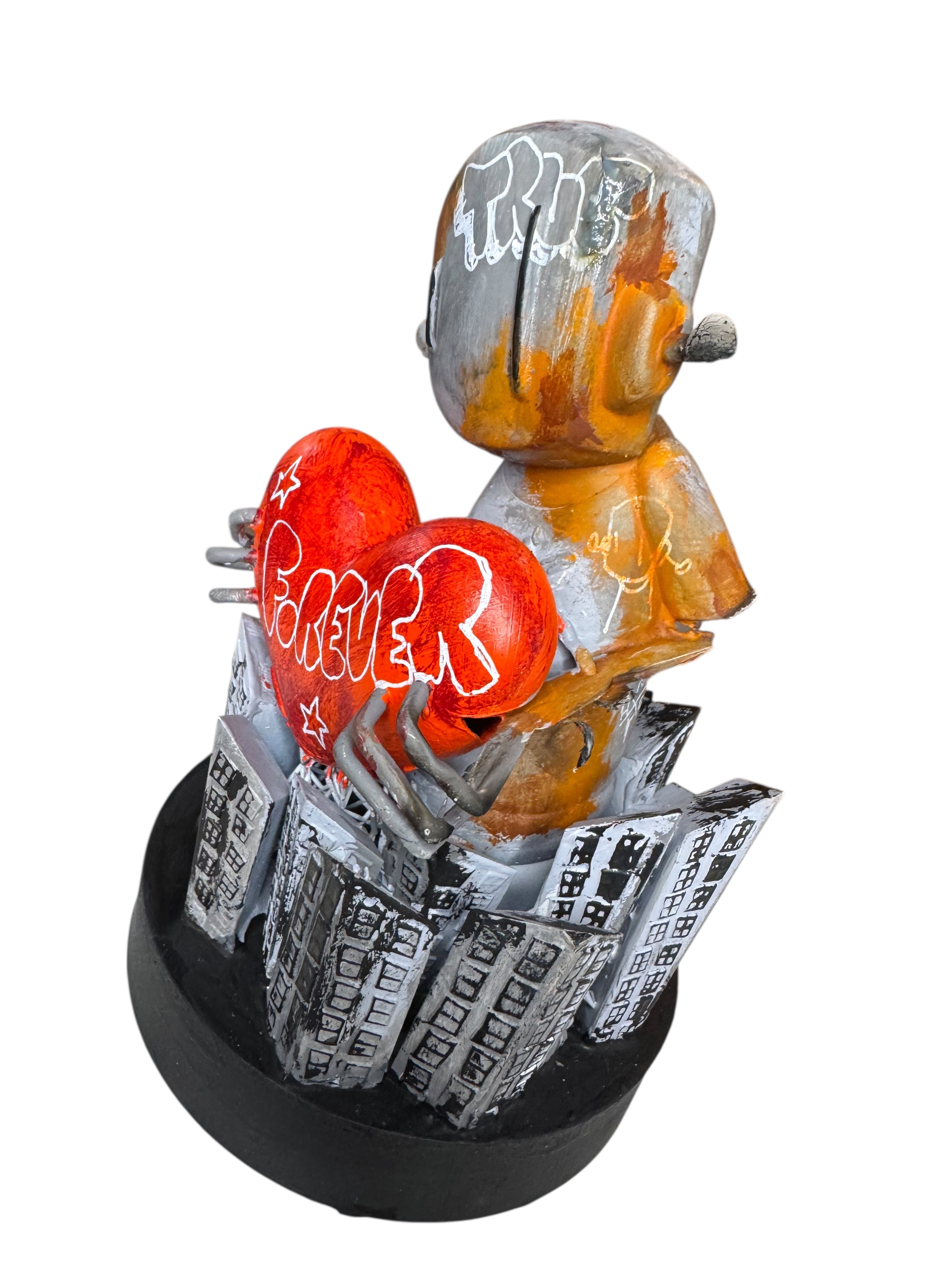 Time Will Tell - Still standing by Chris RWK: A robot-like sculpture holding a red heart with FOREVER, atop a cityscape base, in mixed medium, 6.5 inches tall.
