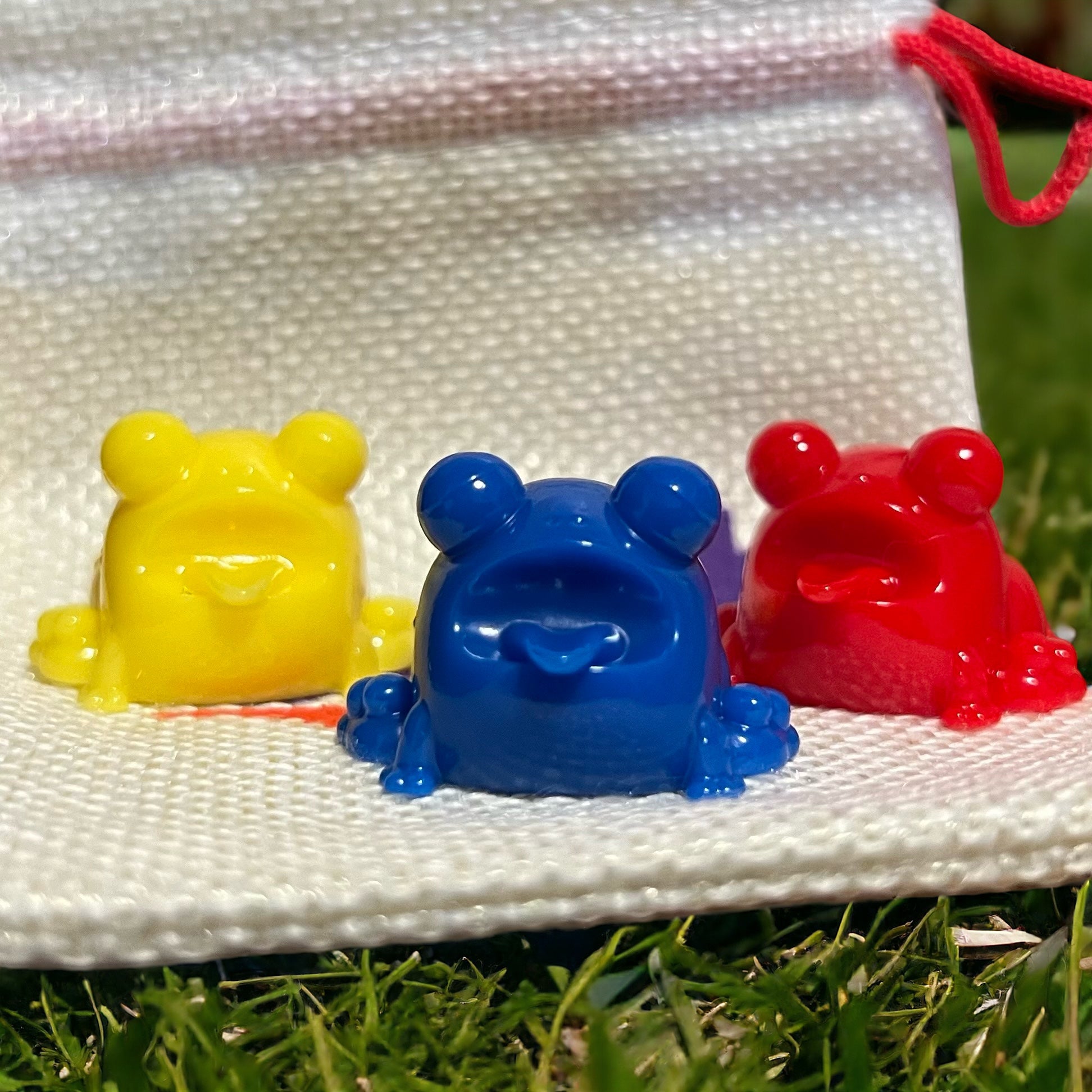Mini Ributts by Leftover Toys: Resin frog toys - blue, yellow, red - on white fabric bag. From Strangecat Toys.