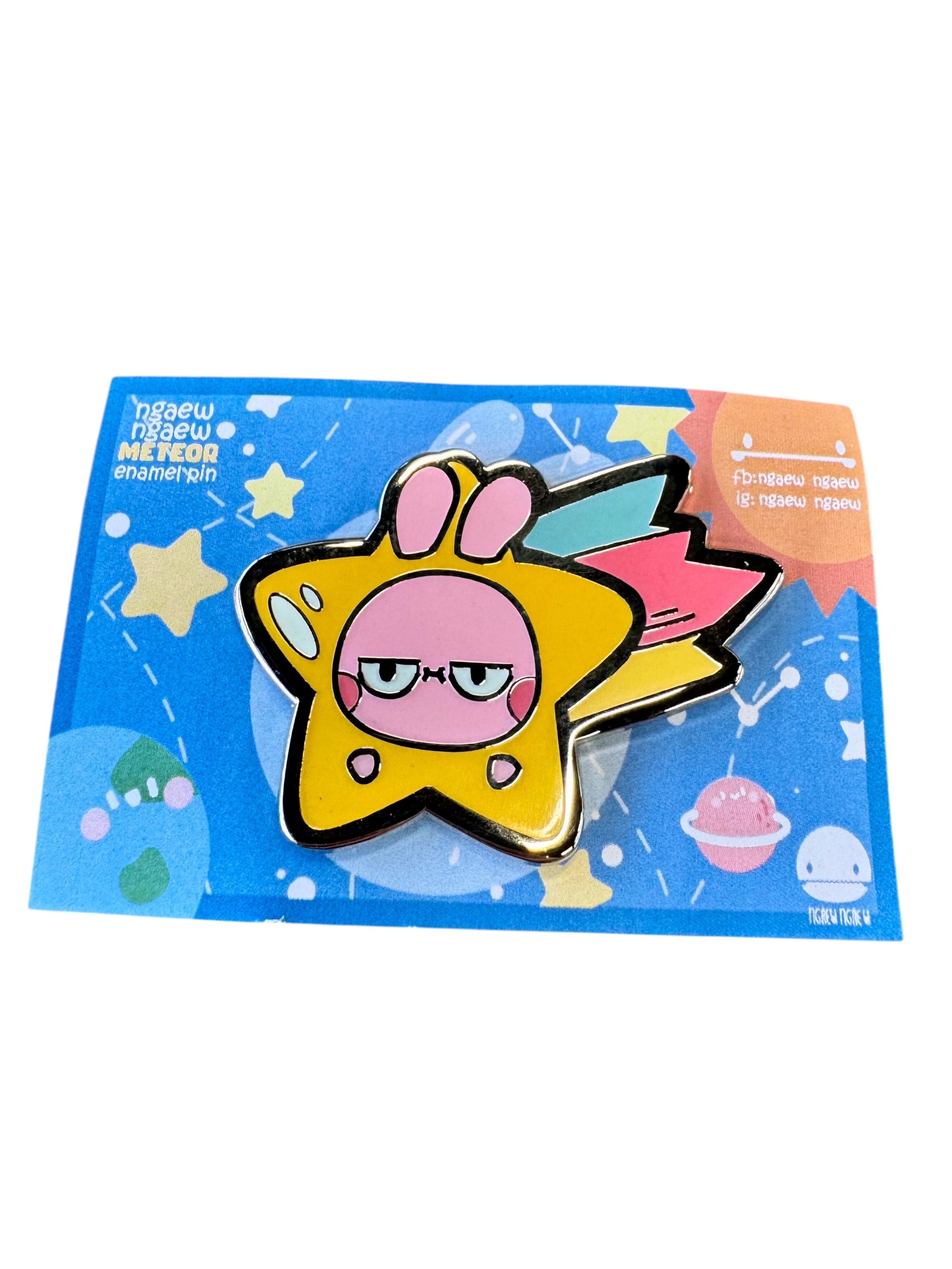 Ngaew Ngaew Meteor Pin featuring a shooting star with a bunny face and rainbow tail, mounted on a celestial-themed backing card.
