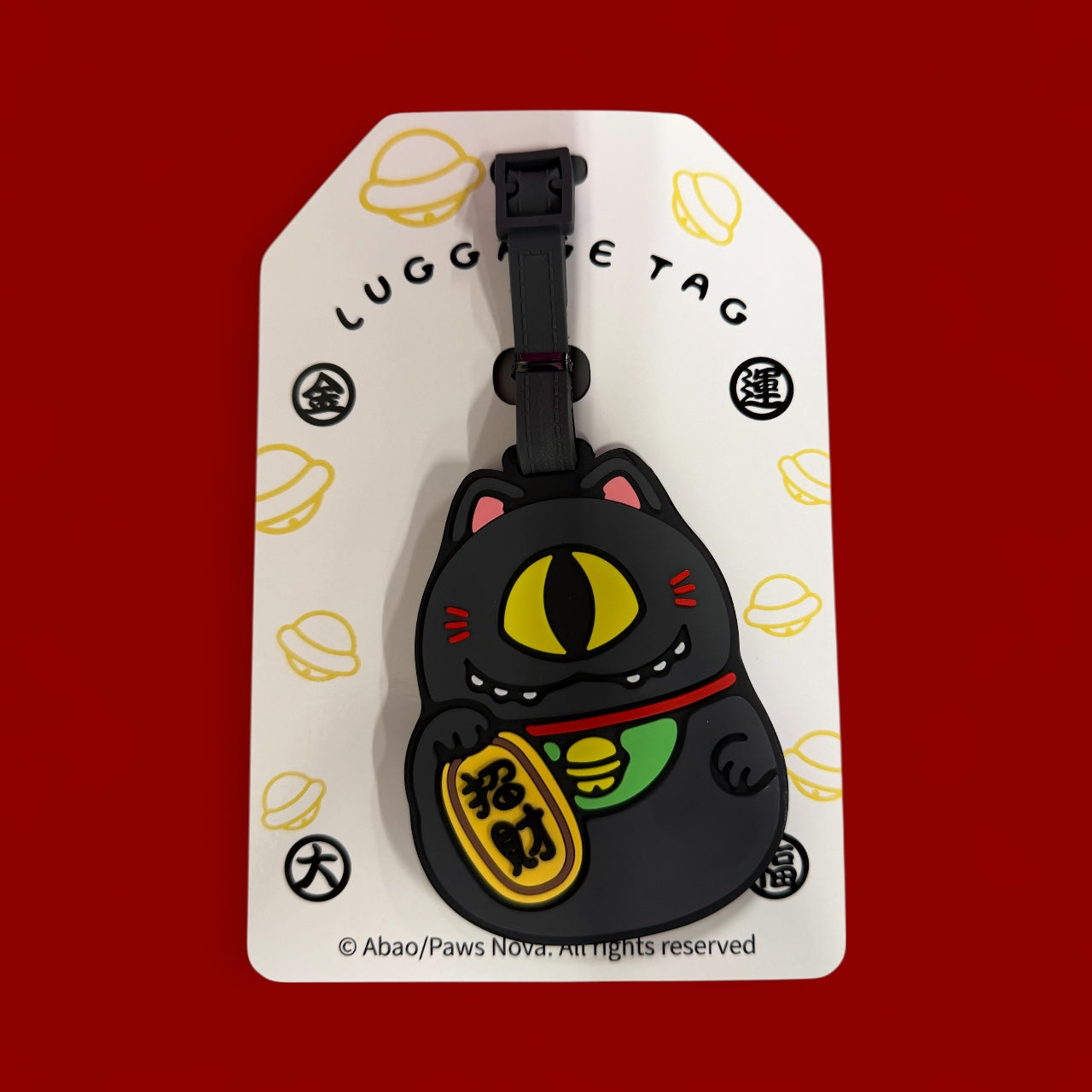 Cat Cat Bug Silicone Luggage Tag featuring a black rubber beckoning cat with a cyclopean eye, holding a wealth-attracting gold token, on backing card with strap.