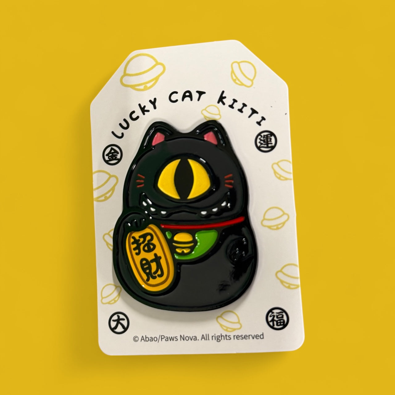 Cat Cat Bug Metal Badge: Glossy black enamel pin of a stylized maneki-neko with yellow cat-eye, red collar, holding a gold fortune token on display card.