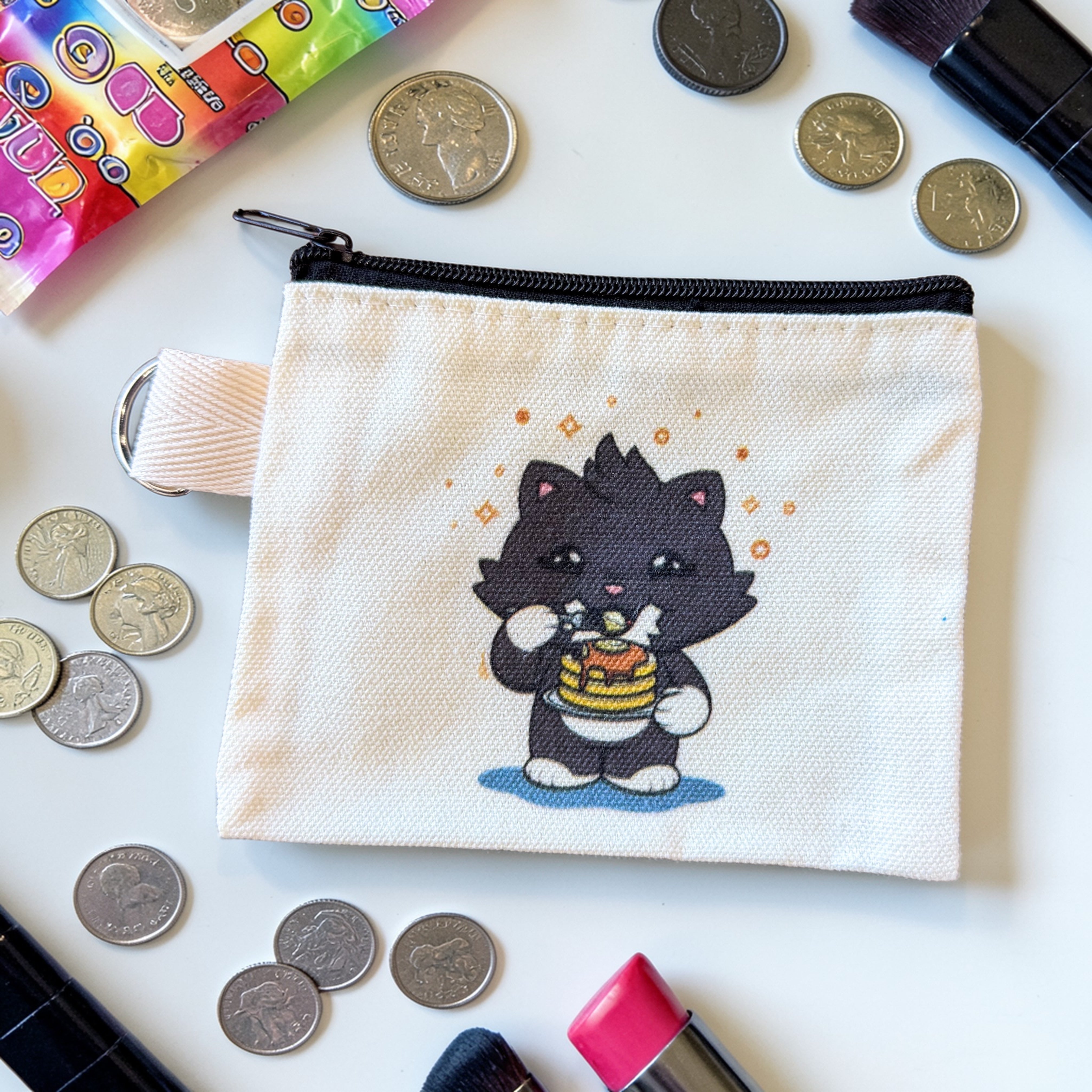 Grandpa Loves Pancakes Zipper Pouch with black cat cartoon, surrounded by coins, pink lipstick, makeup brushes, and candy packaging, on a white surface.