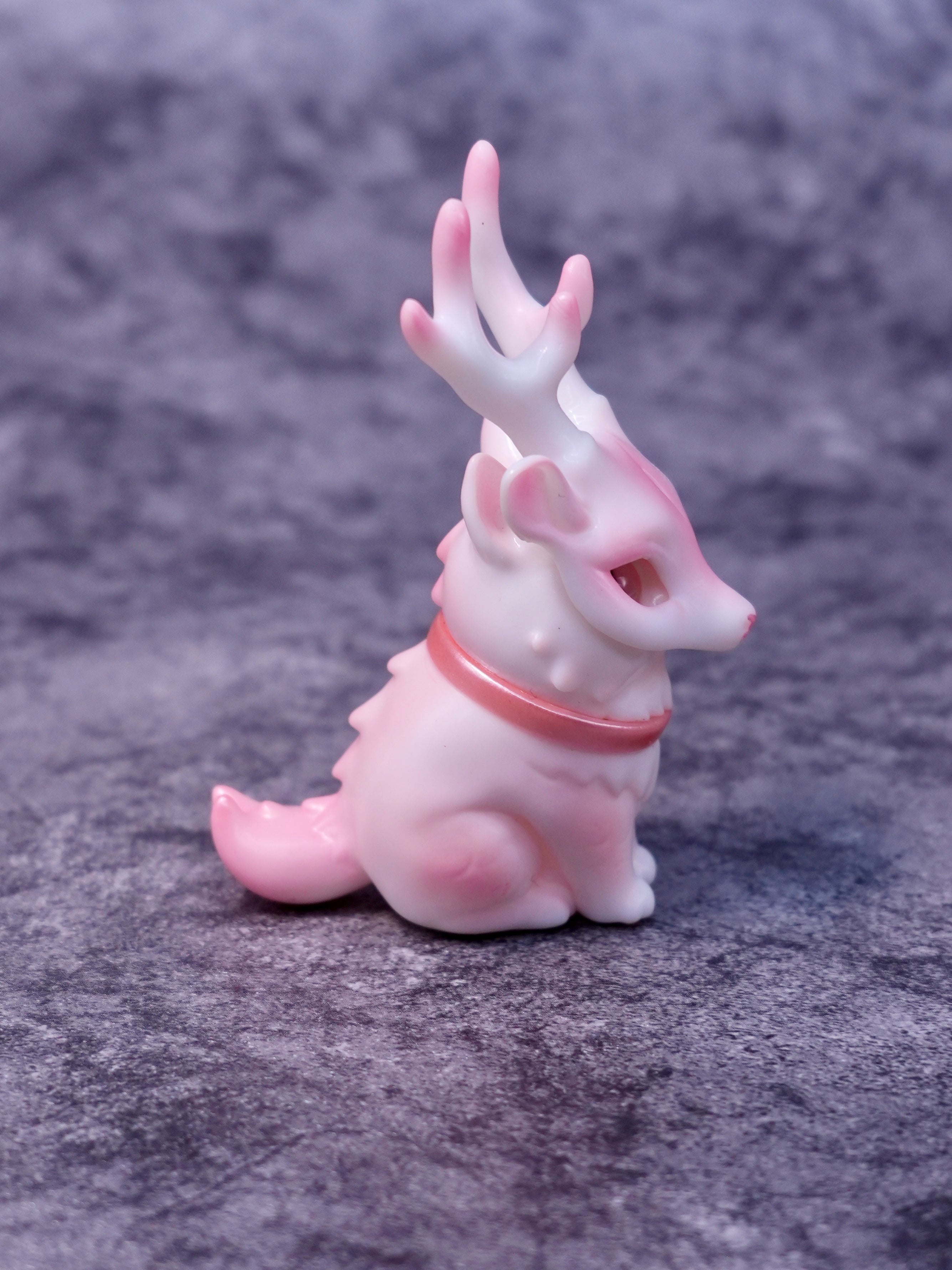 Pink Deer Cat by HOTRU, a pastel-pink vinyl and resin fantasy figurine with antlers, rotatable head, and magnetically attached mask, on a gray fabric surface. Preorder available.