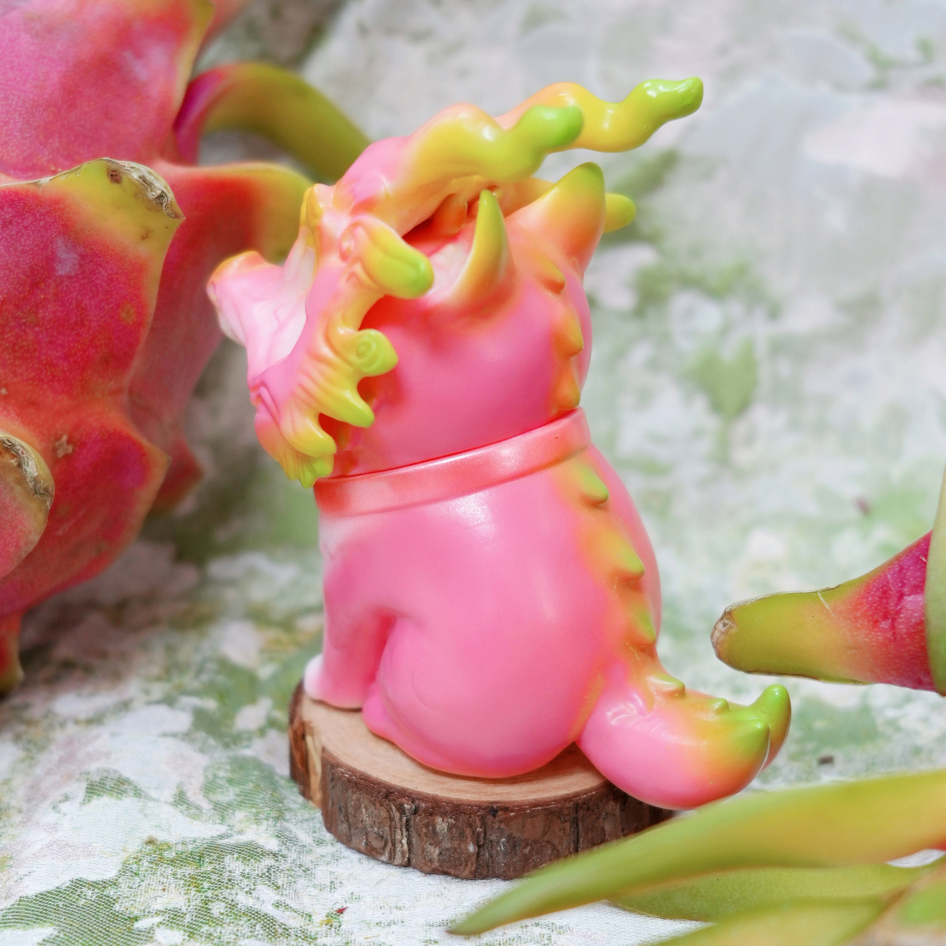 Pitaya Loong cat figurine by HOTRU, a bright pink dragon-dog fusion with a resin mask, seated among dragon-fruit, for preorder at Strangecat Toys.