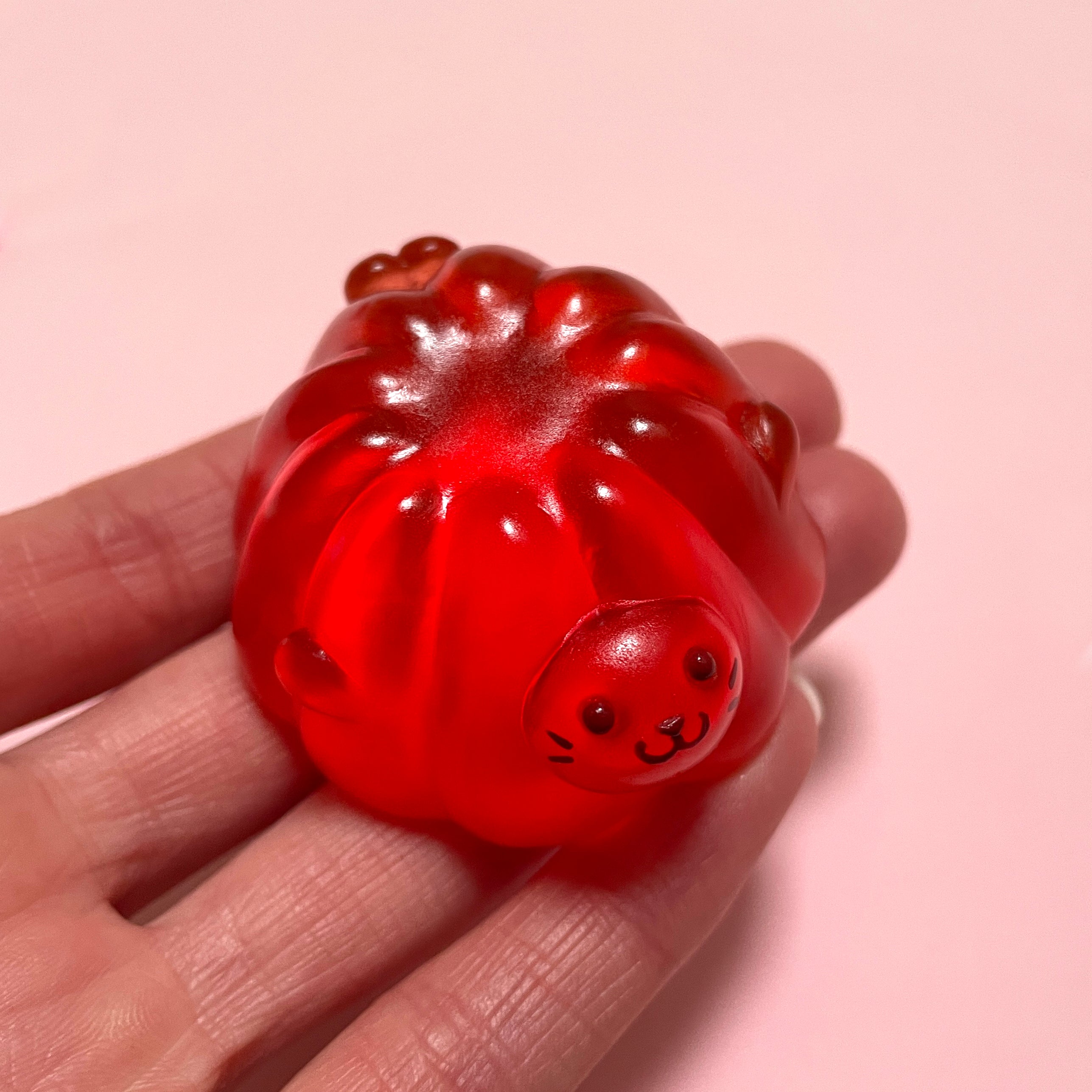 A hand holds a red jelly bear resin figure, part of Little Shit Big Deal - Jelly Seals by Little Blue Seal. Dimensions: 1” H x 1 ¾” W x 1 ¾” L. Ship 28 days post-show opening.