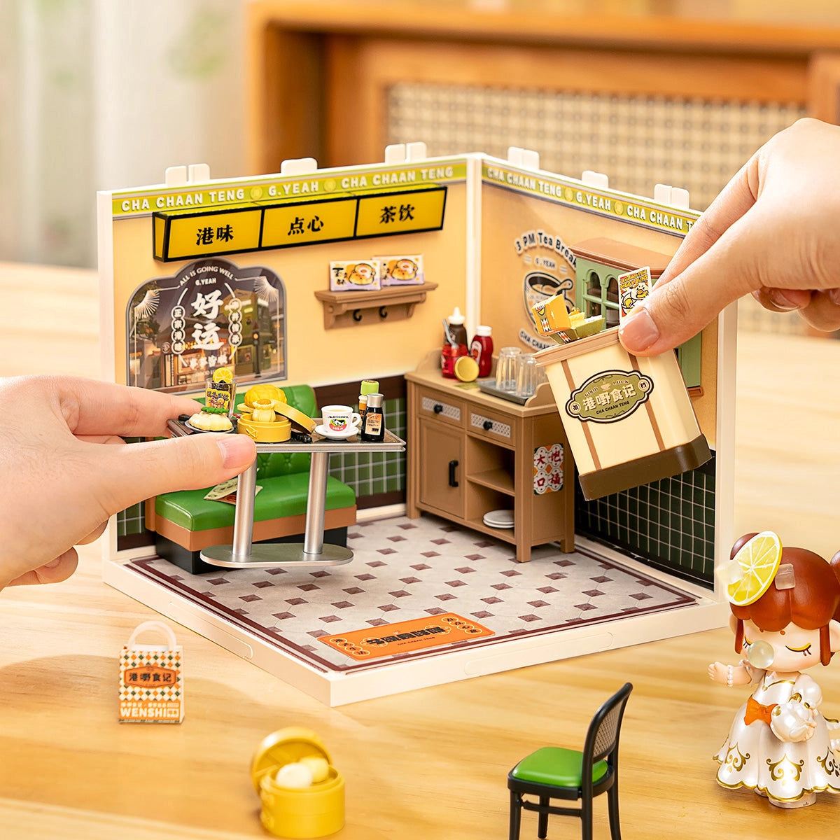 Rolife Super Creator Miniature House - Hong Kong Bites Cafe DW021: Hands assembling a detailed diorama of a Hong Kong tea café with miniatures and a collectible character figurine.